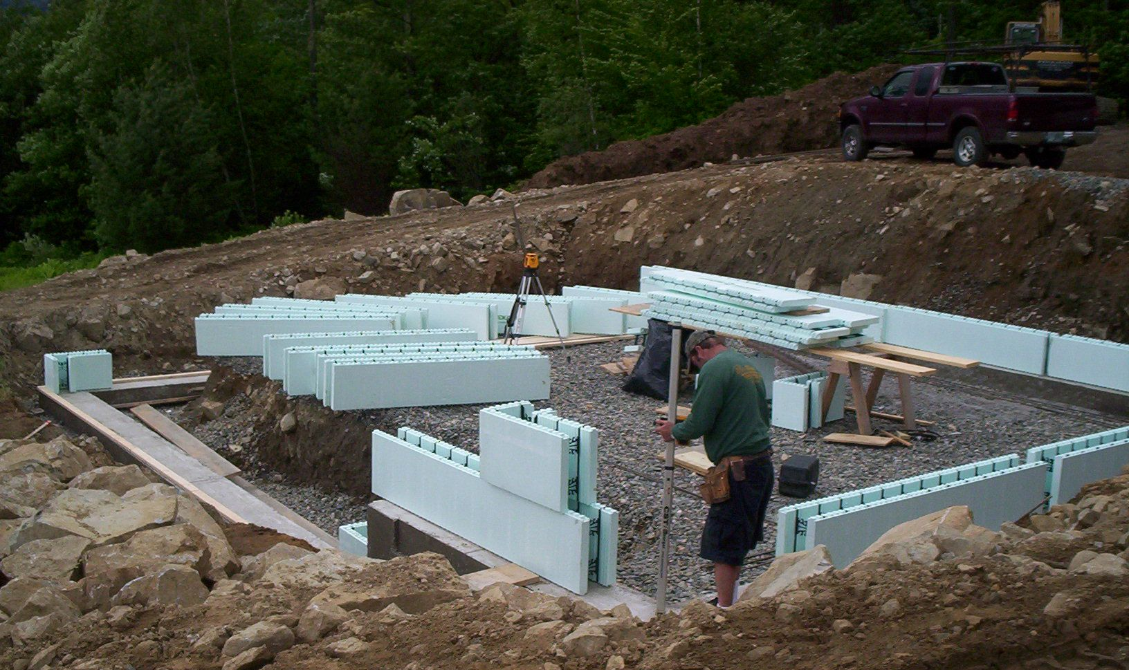 Construction site with foundation walls being built from white blocks on a dirt lot.