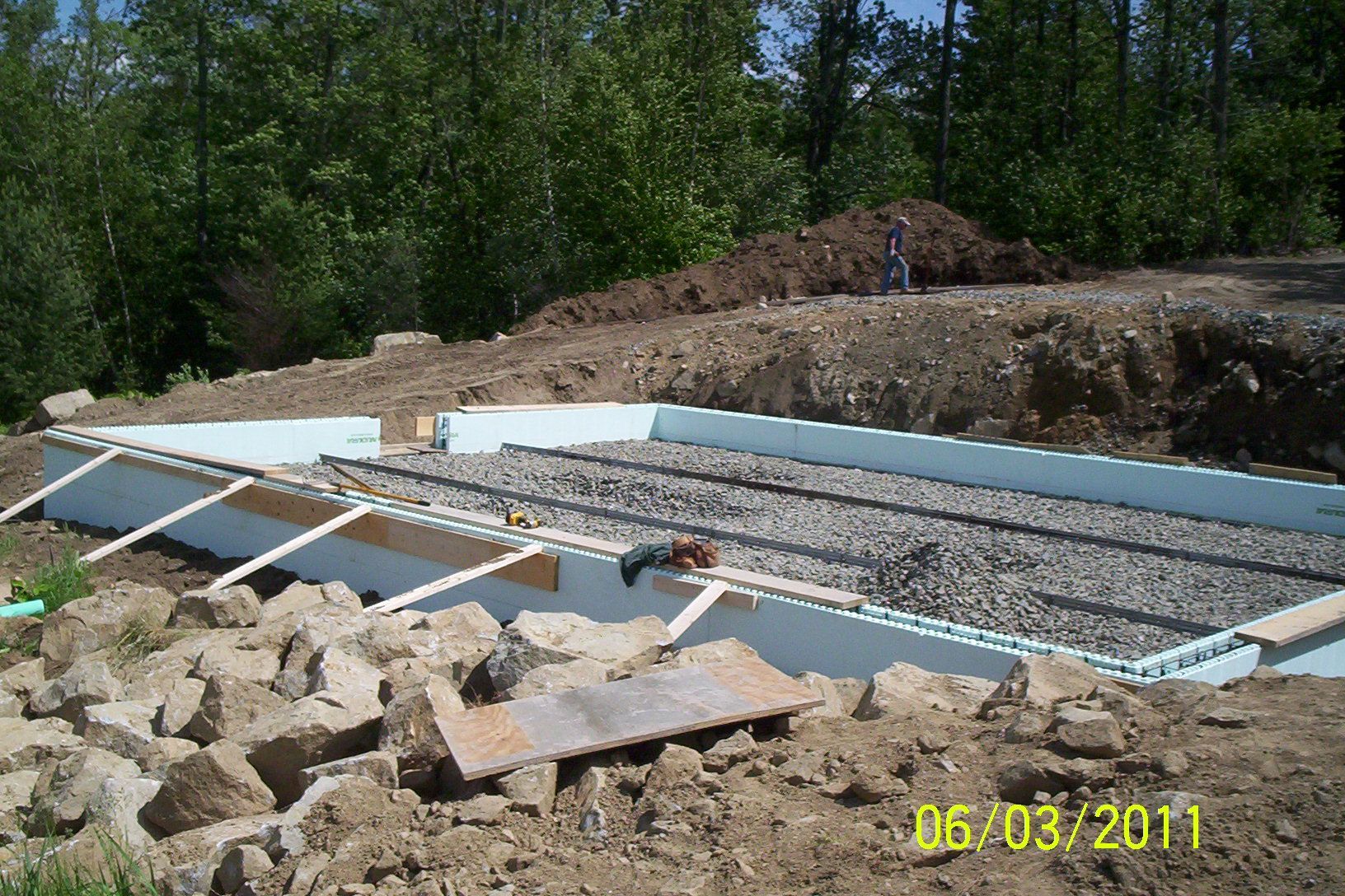 Partially built foundation with gravel, concrete forms, and scattered construction debris outdoors