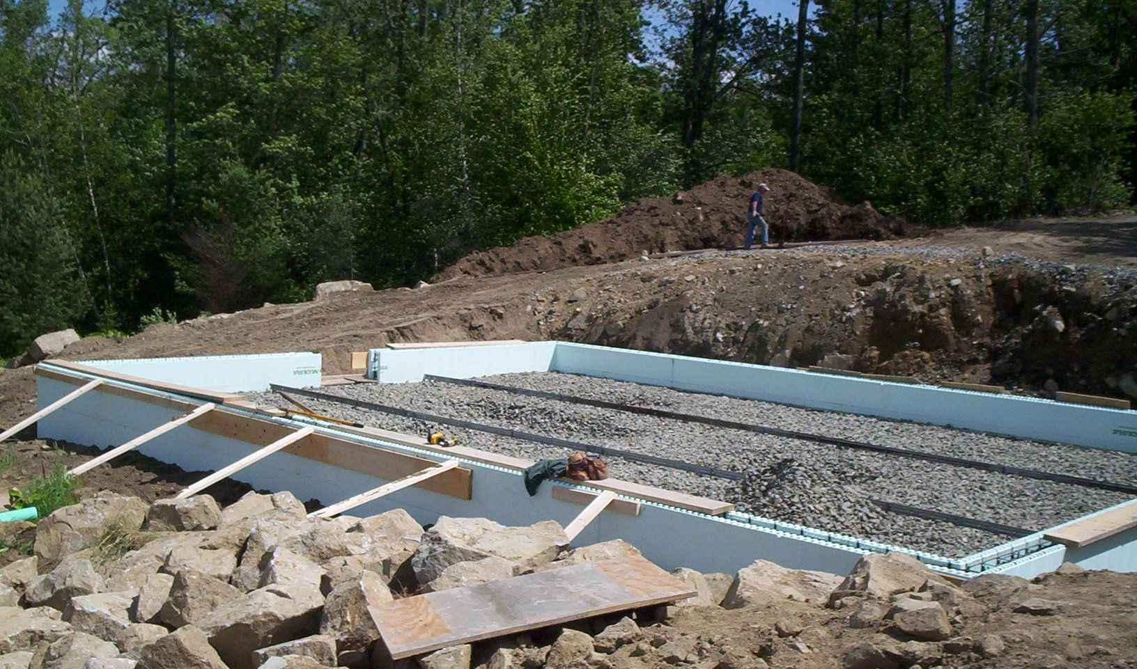 Concrete foundation under construction with rebar, white forms, and gravel in a wooded area