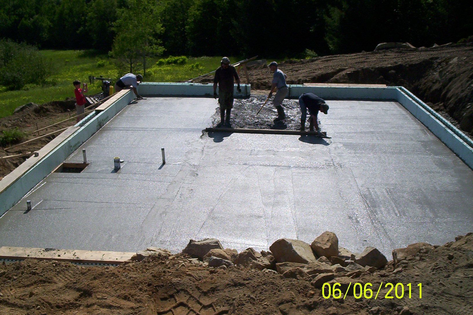 Workers smoothing concrete on a large rectangular slab foundation outdoors