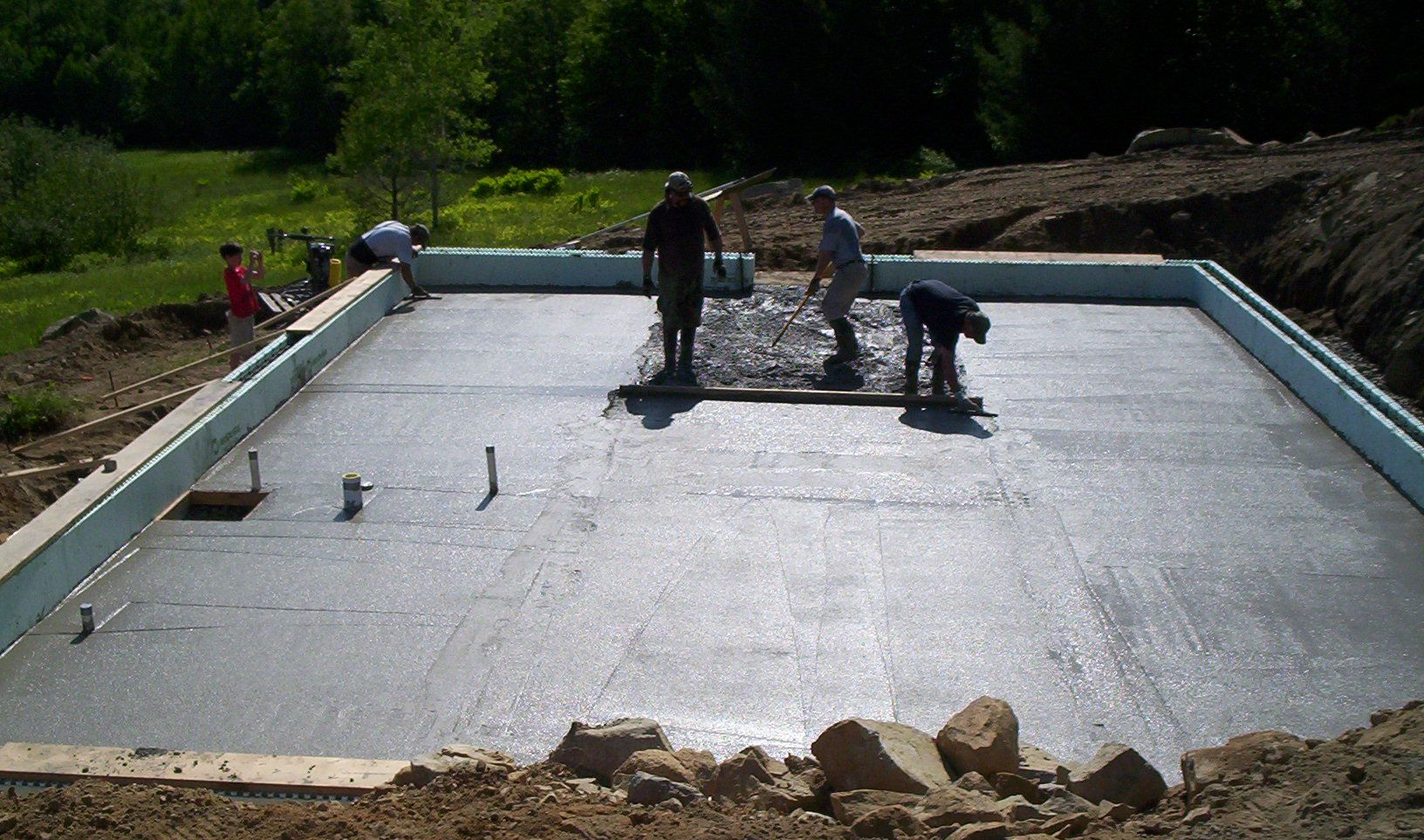 Workers smoothing wet concrete on a rectangular foundation slab at a construction site outdoors