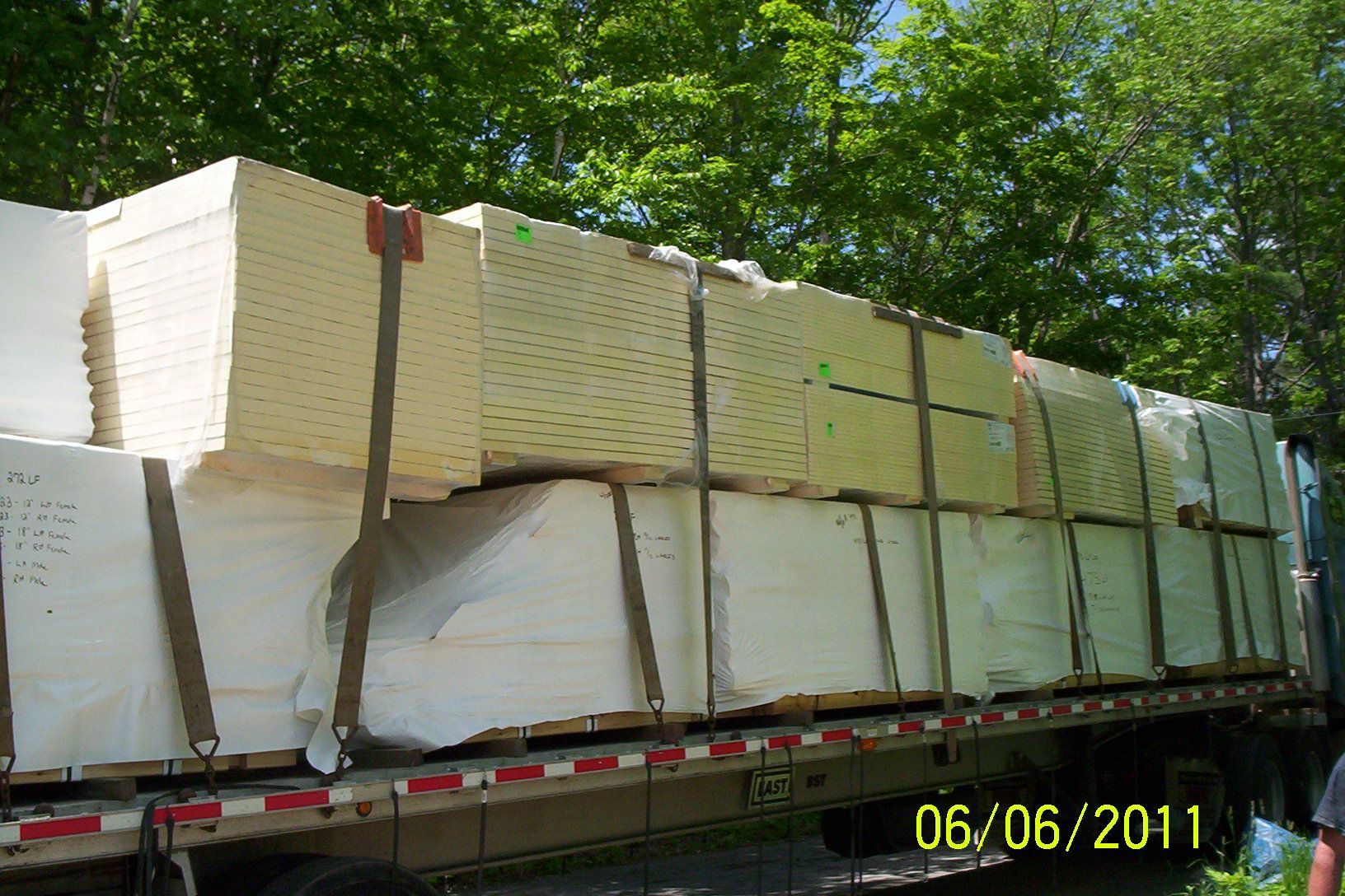 Stacked white bundles secured on a flatbed truck, with trees in the background.