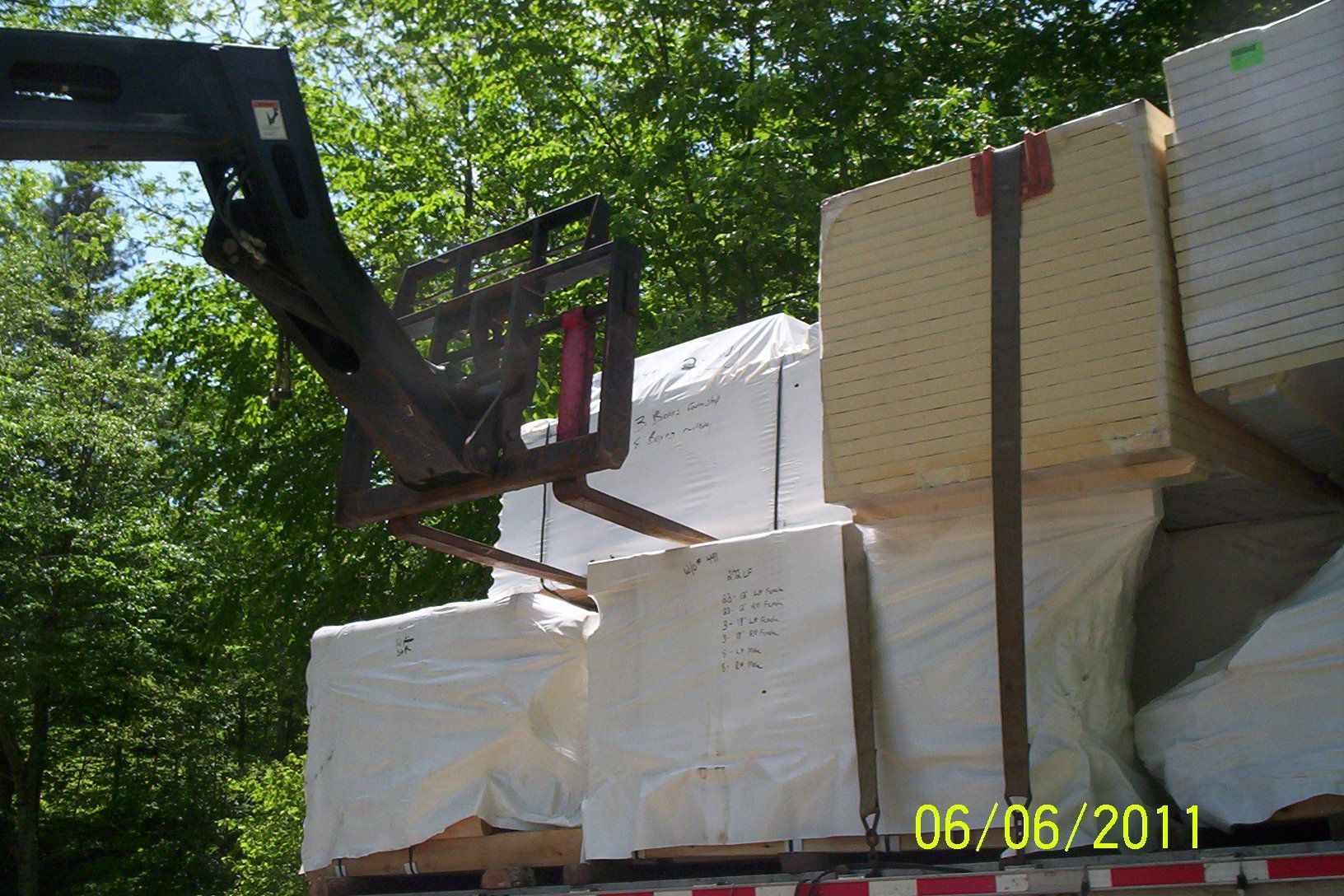 Forklift unloading white foam blocks on a flatbed truck in a wooded area