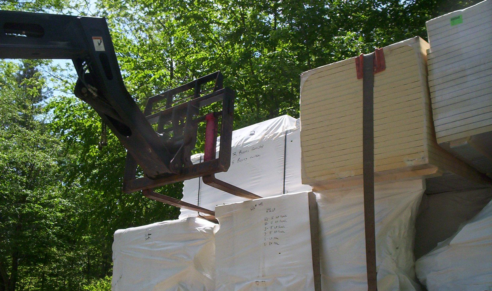 Forklift lifting stacked white foam crates outdoors beside trees
