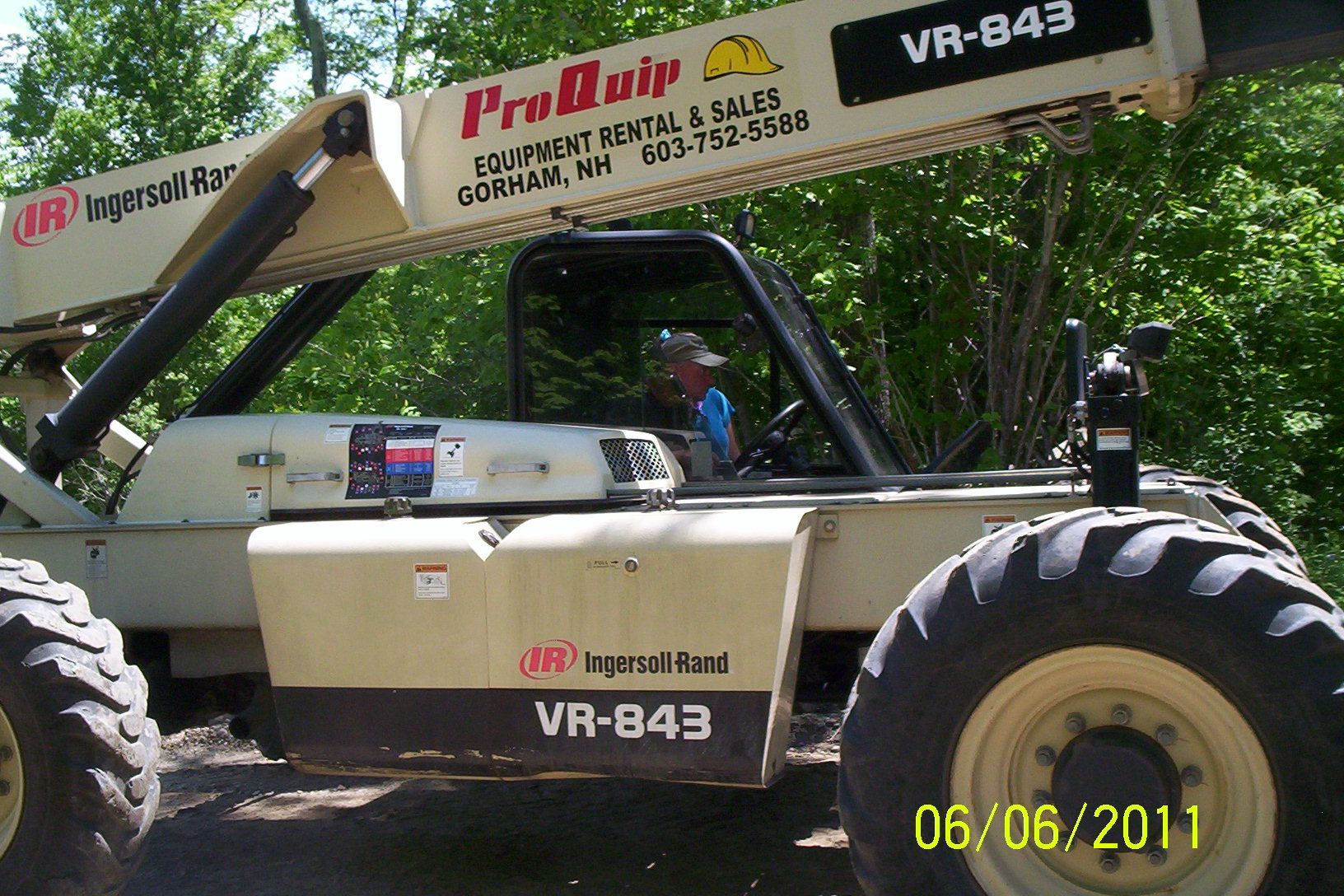 Beige off-road utility vehicle with a crane arm parked in a wooded area.