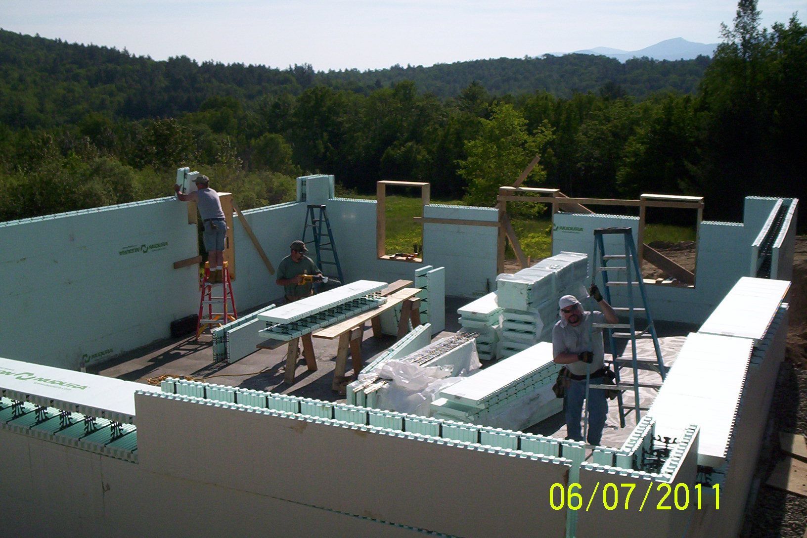 Construction site with white walls and workers installing roof panels under a sunny sky