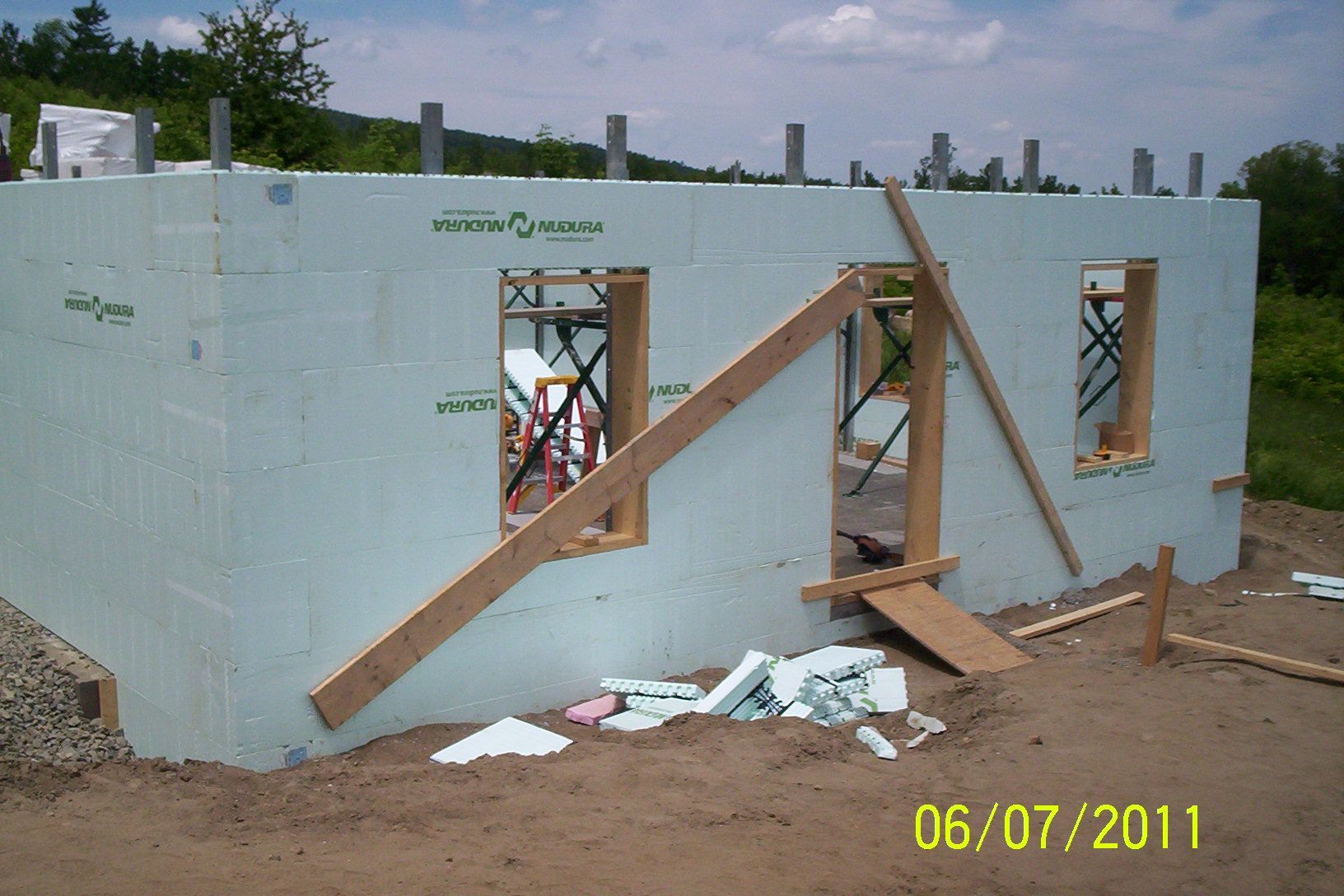 Unfinished house with blue walls, wooden braces, and window openings on a dirt lot under construction.
