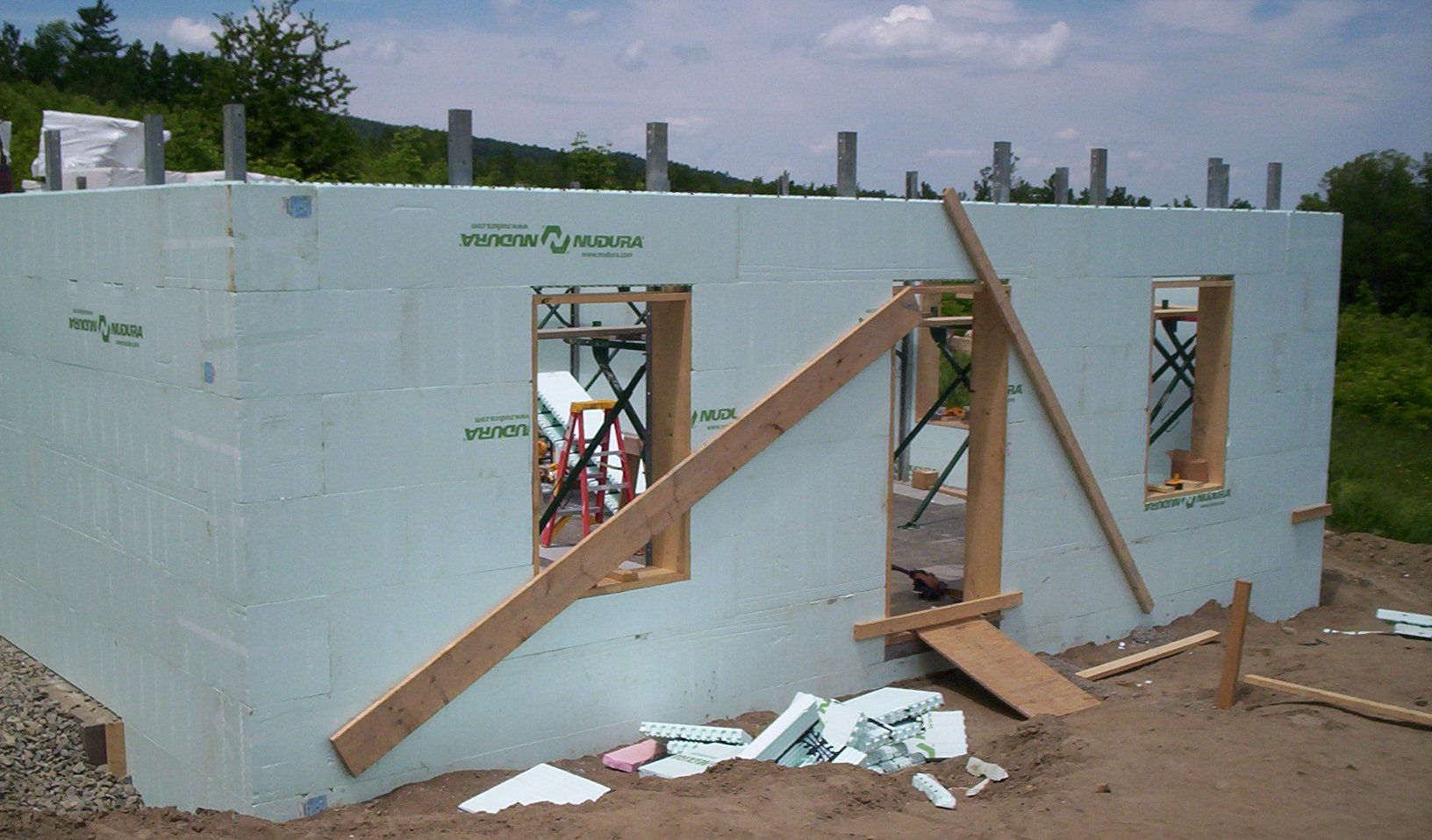 Partially built house with pale blue walls, window openings, and wooden braces at a construction site