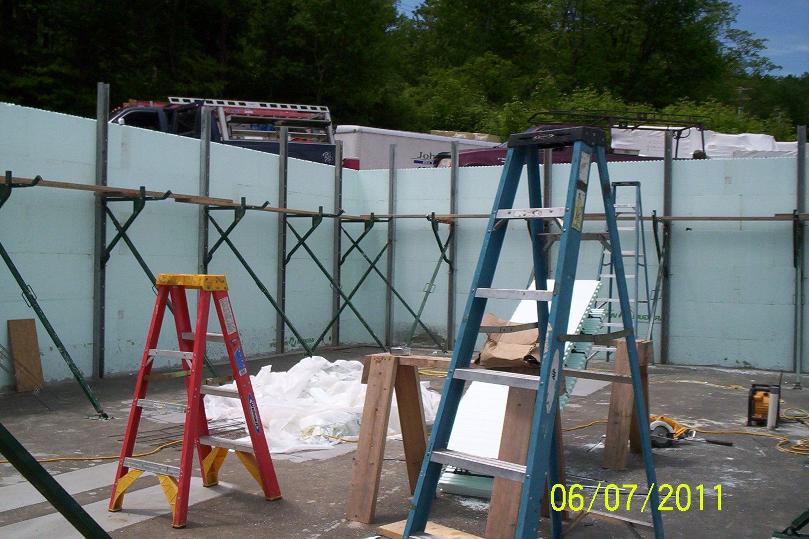 Construction site with blue and red ladders inside a partially built white wall structure.