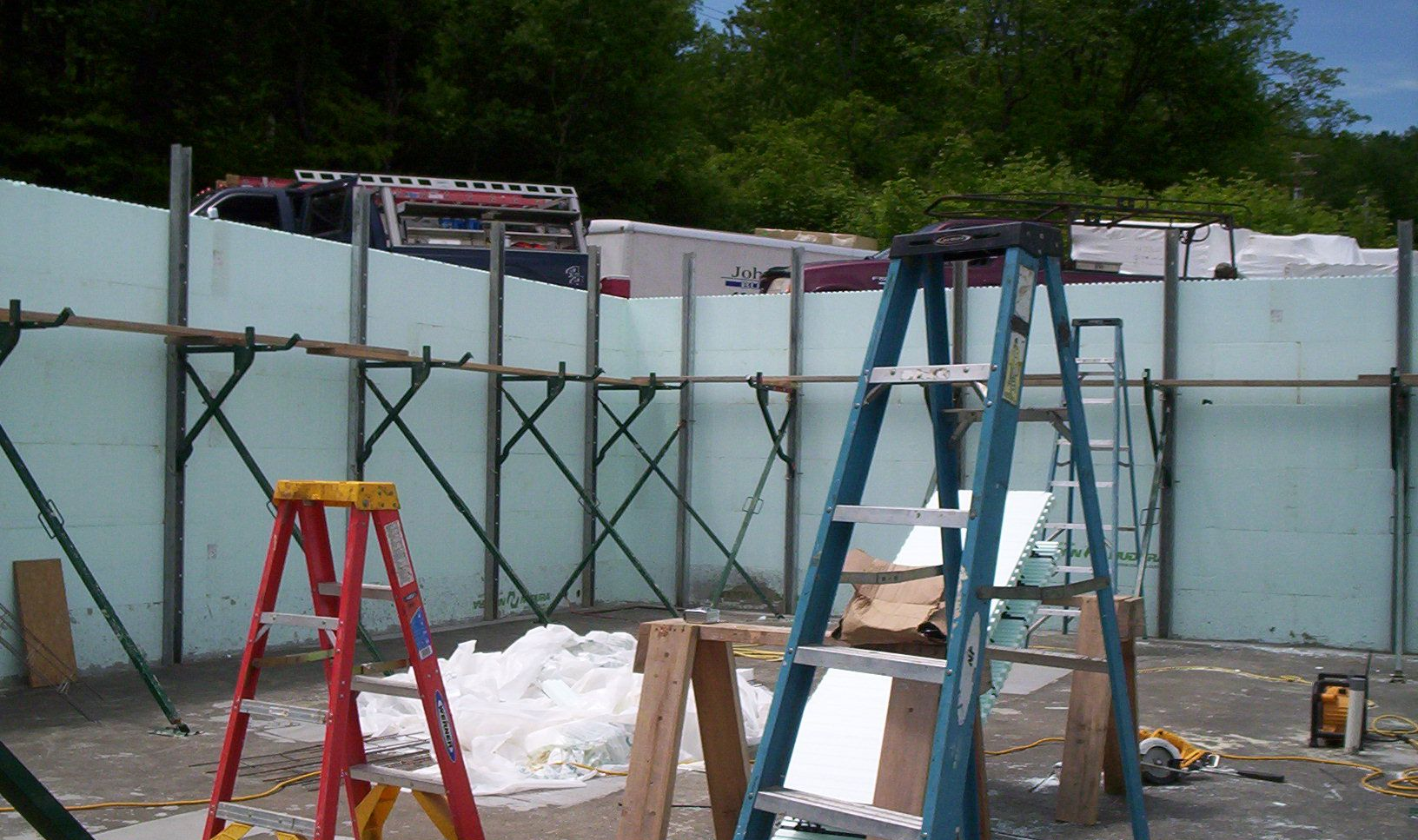 Construction site with blue fence panels, ladders, and building materials in an outdoor area