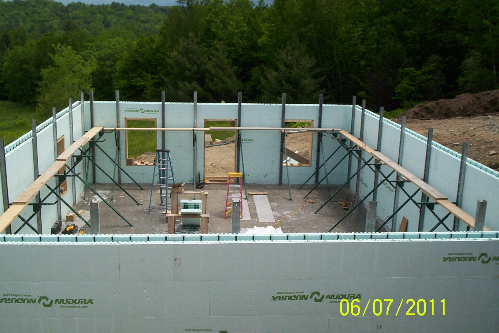 Concrete foundation walls under construction with metal bracing and forested background