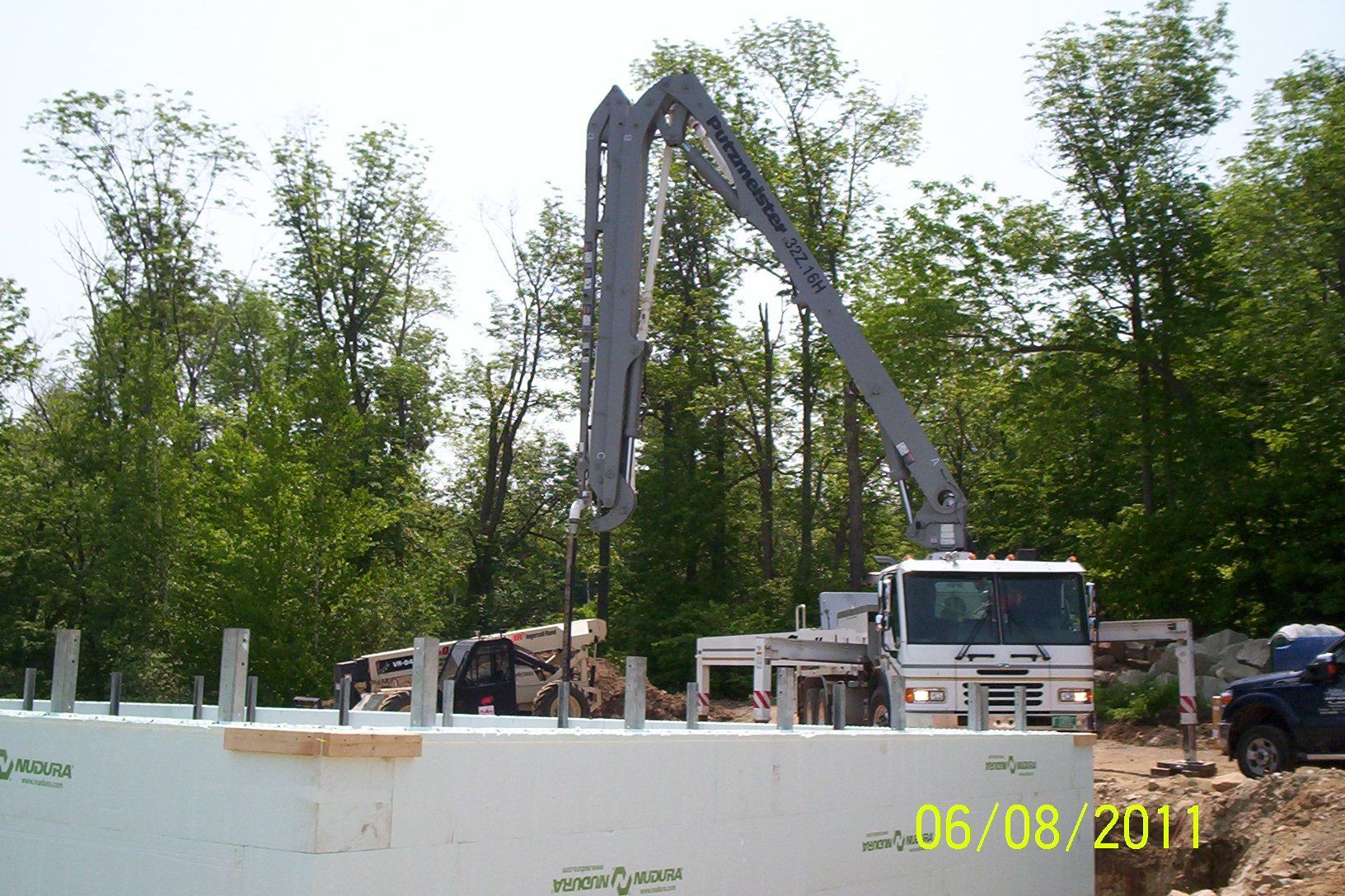 Excavator at a construction site behind a white barrier, with trees in the background.
