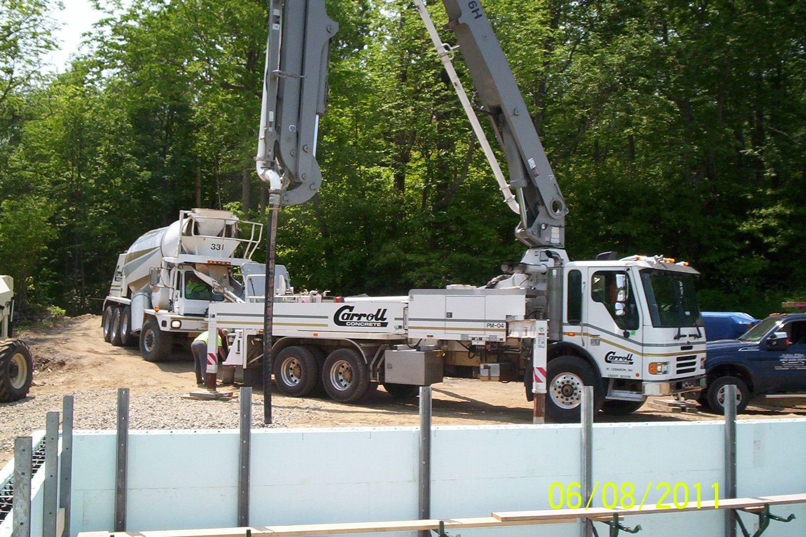 Concrete pump trucks at a construction site with two raised boom arms surrounded by trees