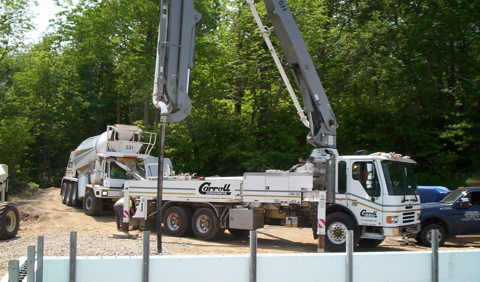 Concrete pumps and trucks at a construction site with raised boom arms, surrounded by trees.