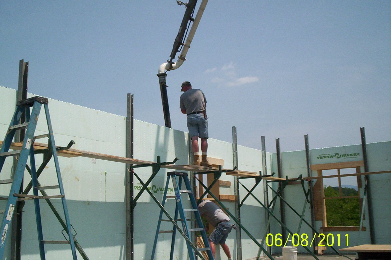 Workers on scaffolding lifting a wall panel with a crane at a construction site