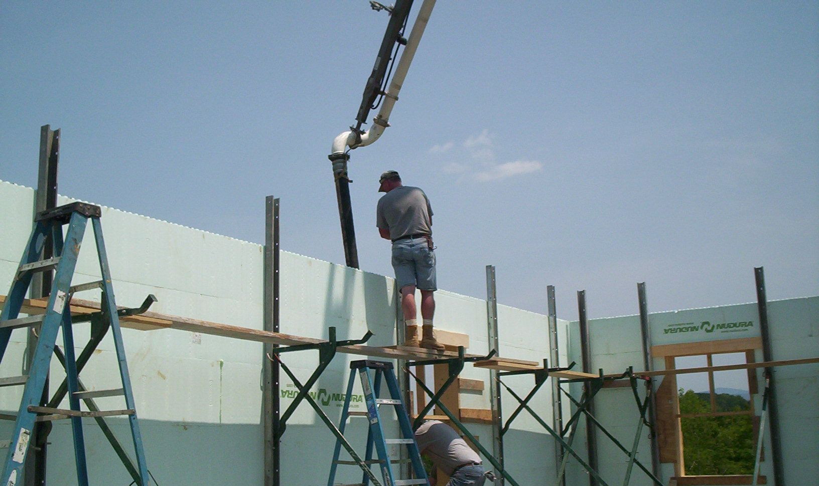 Worker on scaffolding lifting a panel with a crane at an outdoor construction site