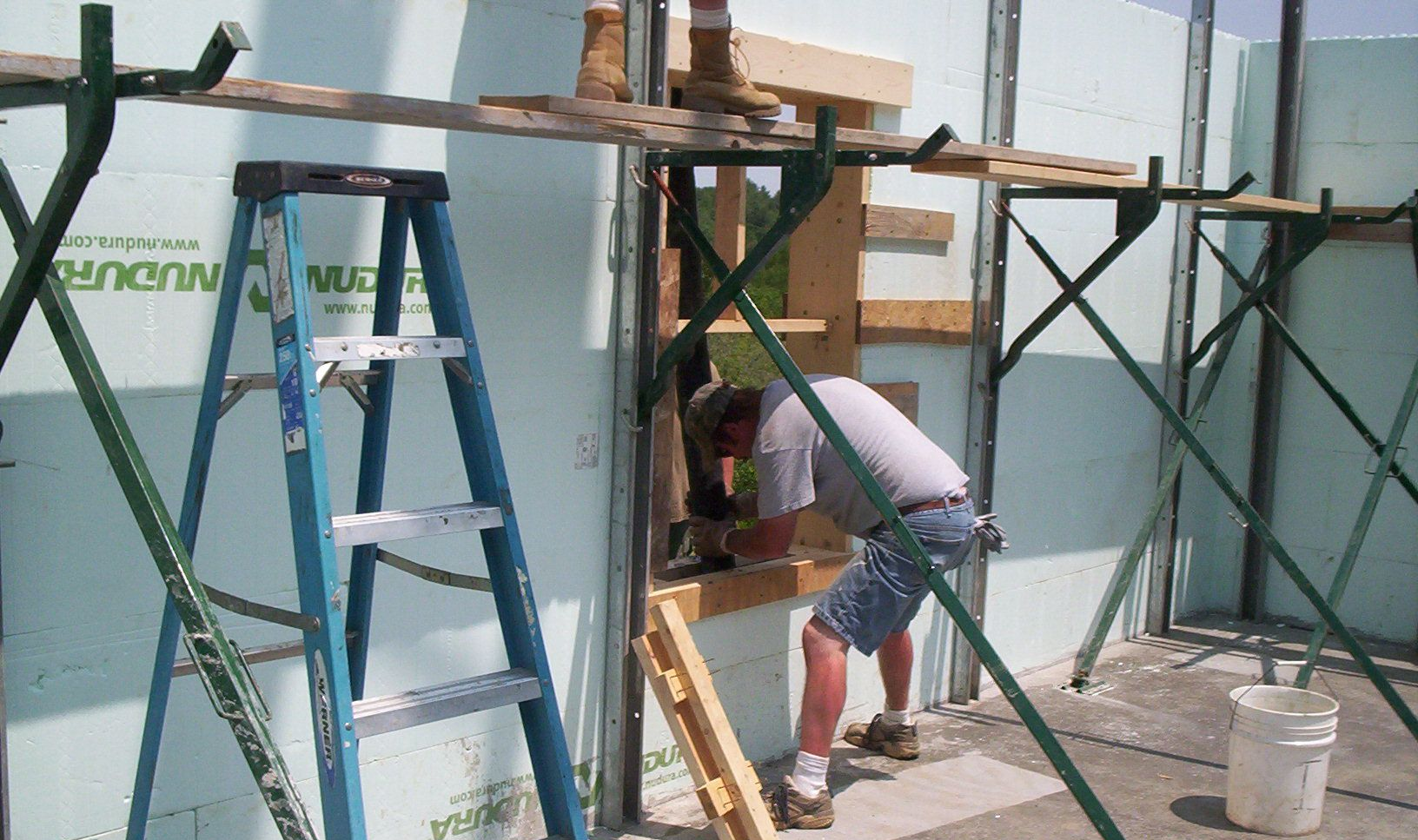 Worker using a sander at a construction site beside ladders and scaffolding.