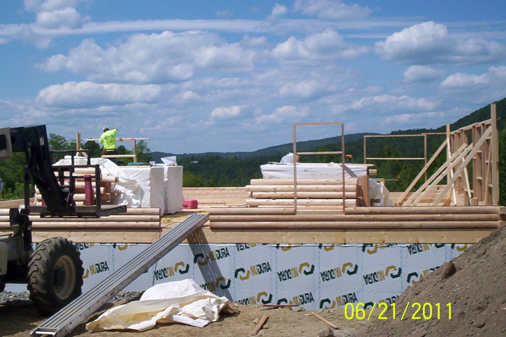Construction site with lumber stacks, forklift, and framed walls under a cloudy sky