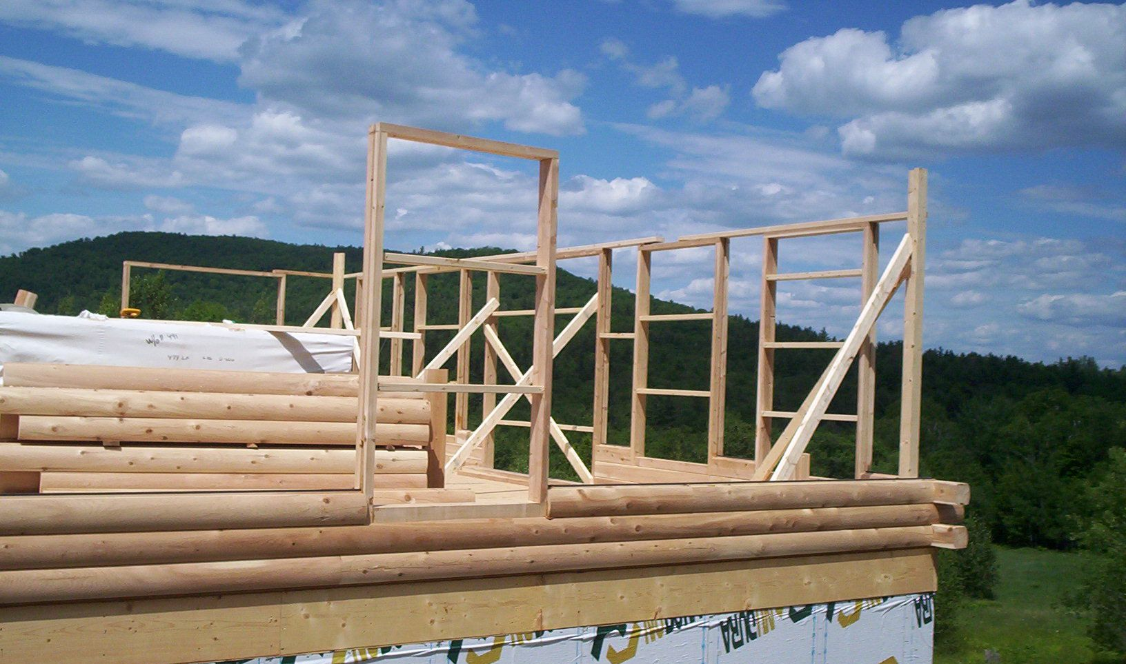 Partially framed log cabin under construction with stacked logs and wooden supports against a cloudy sky