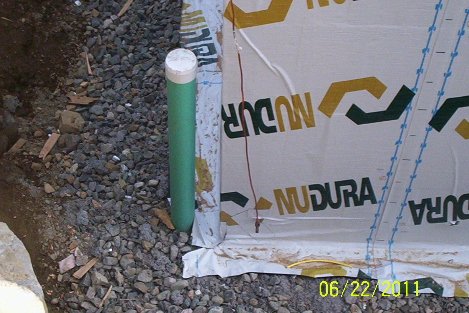 Green capped pipe beside wrapped foundation wall on rocky ground