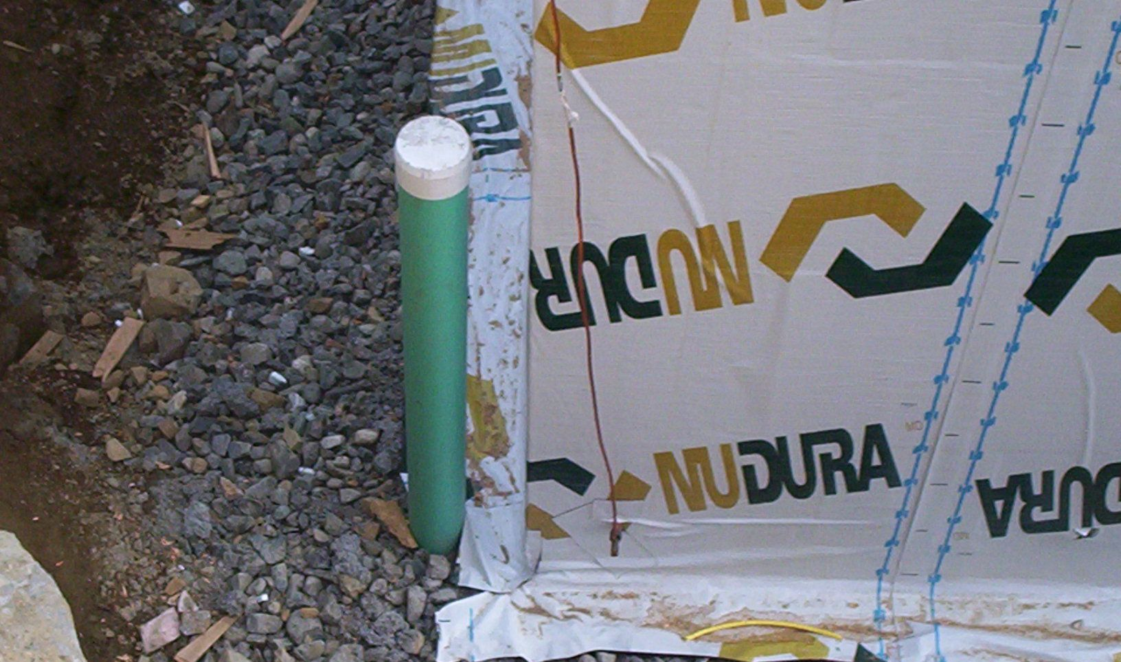 Green utility pipe beside wrapped building materials on gravel ground