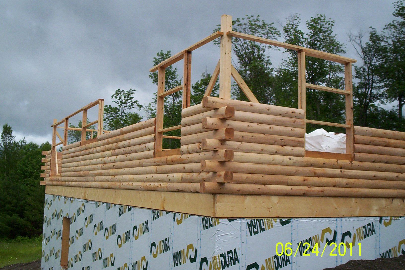Log cabin under construction with log walls and wooden framing on a raised foundation