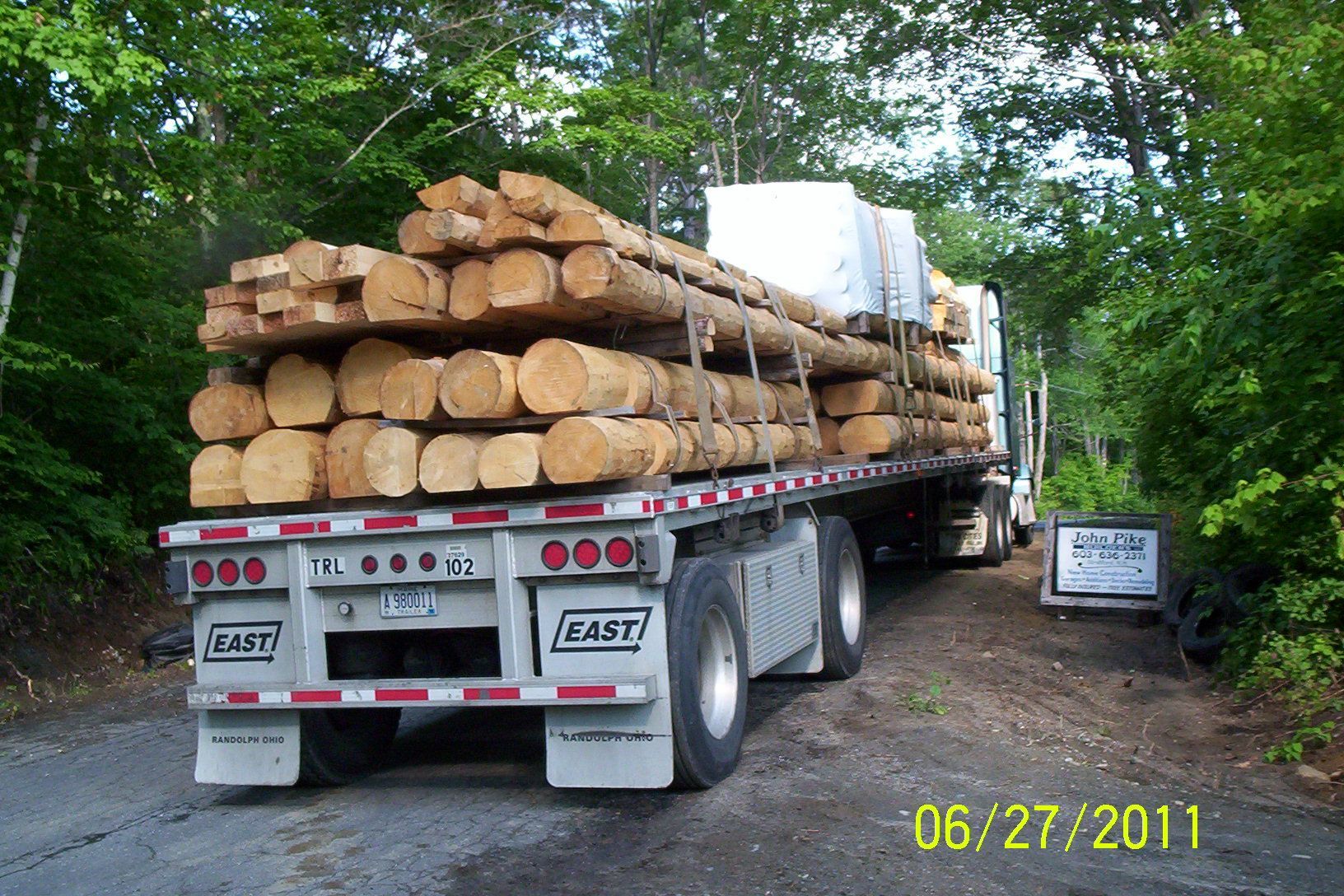 Logging truck loaded with stacked timber on a wooded road, dated 06/27/2011