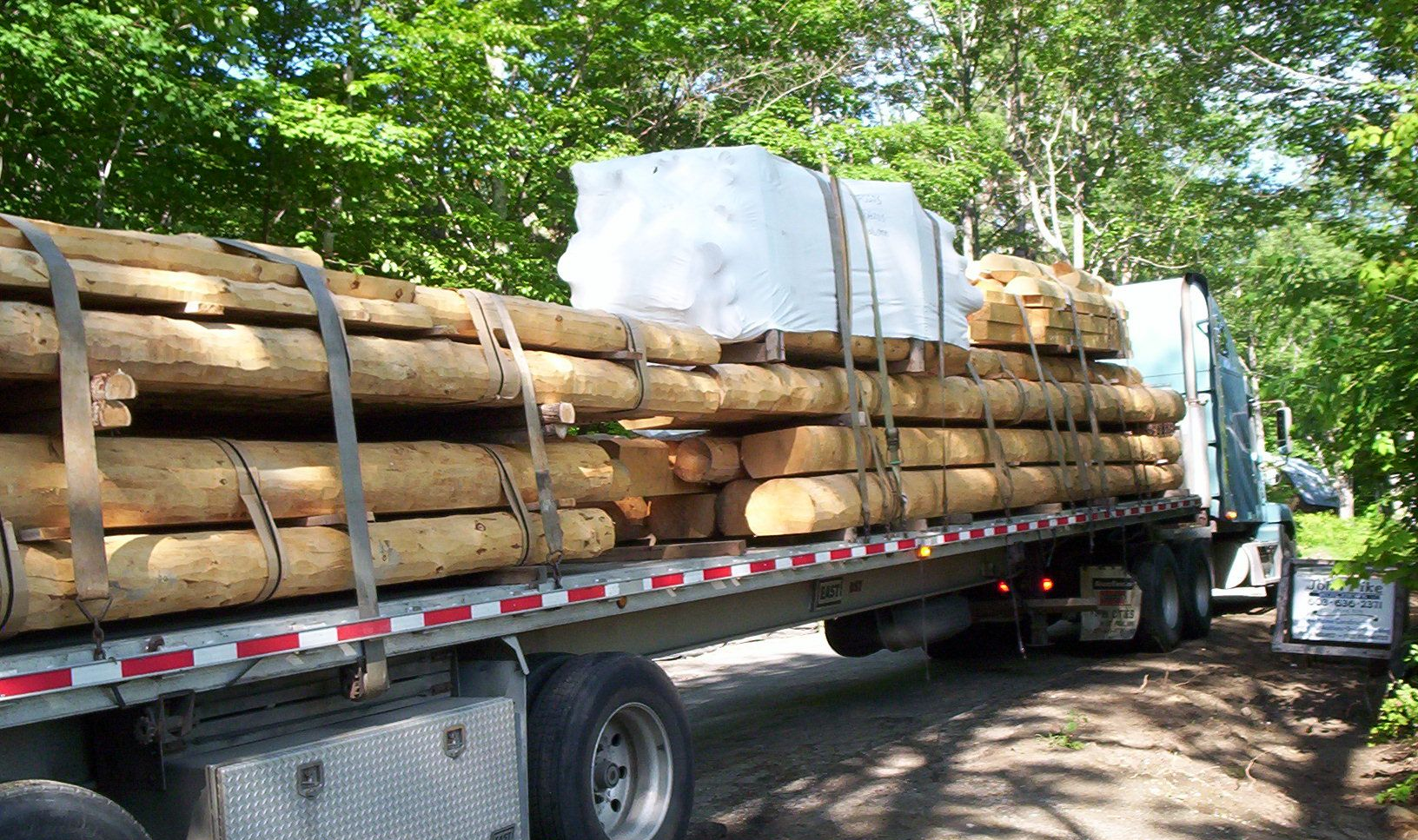 Logging truck loaded with stacked logs and covered bundles on a wooded road