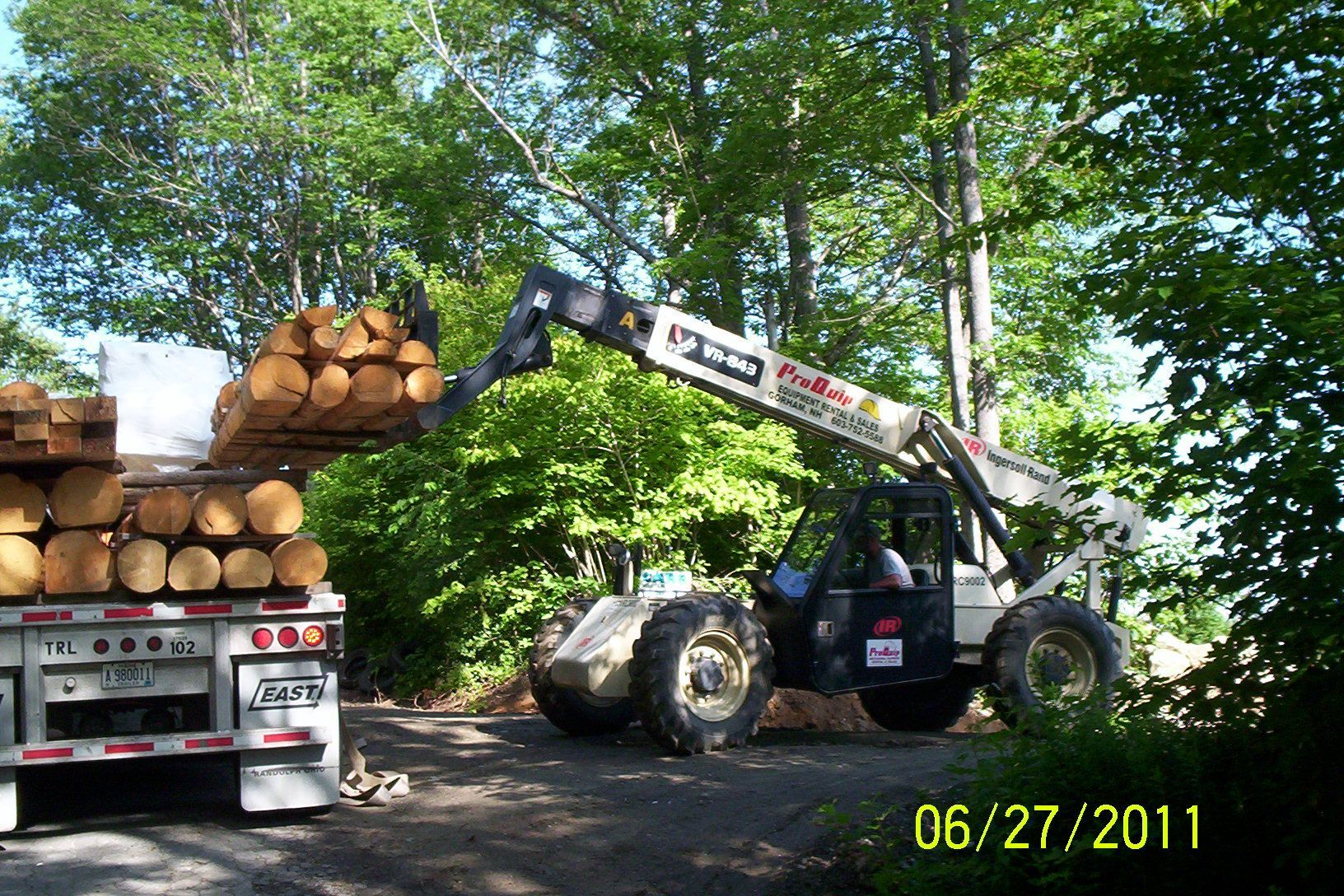 Log loader lifting logs from a truck in a wooded area, dated 06/27/2011