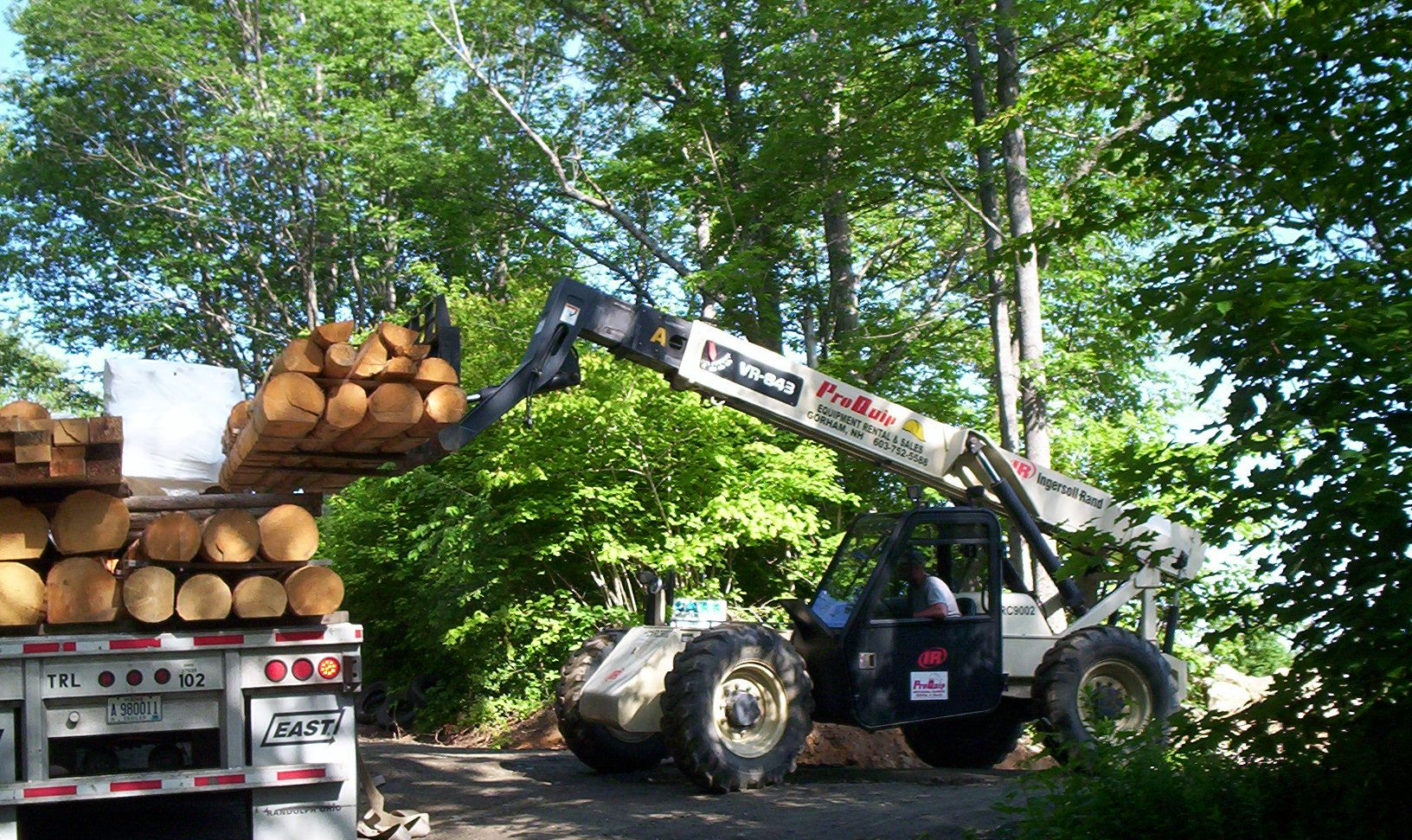 Log loader lifting stacked logs onto a truck in a wooded area