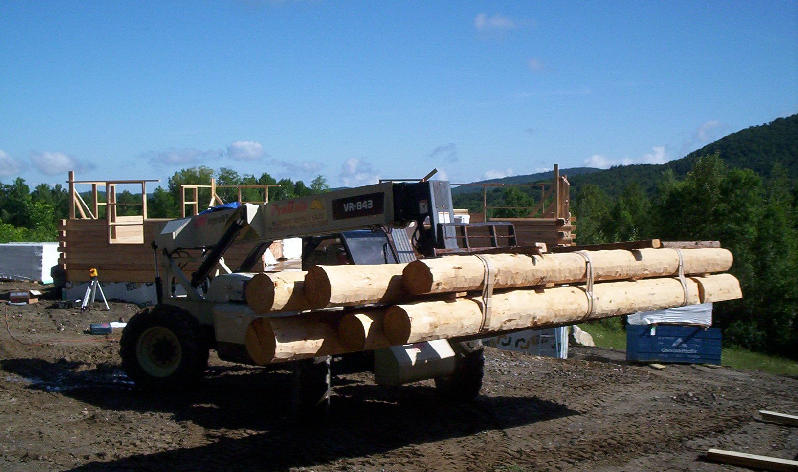 Loader carrying long logs in a lumber yard with mountains in the background