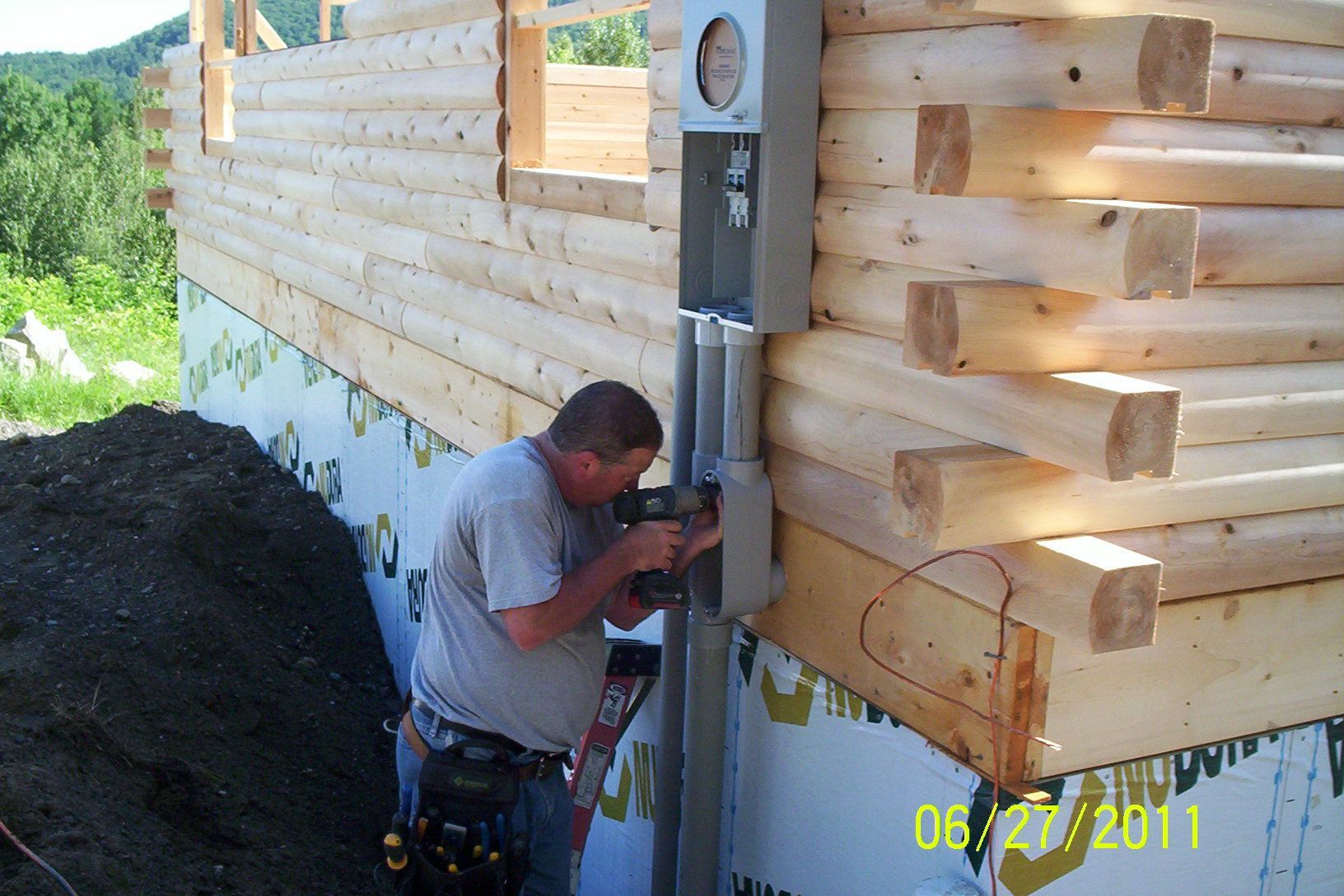 Worker installing a level on a partially built wooden wall beside a house foundation