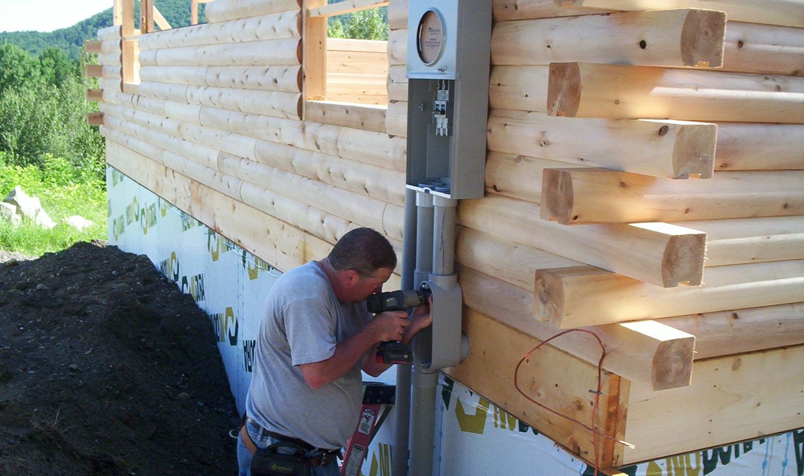 Worker installing electrical meter on the exterior of a wooden house under construction