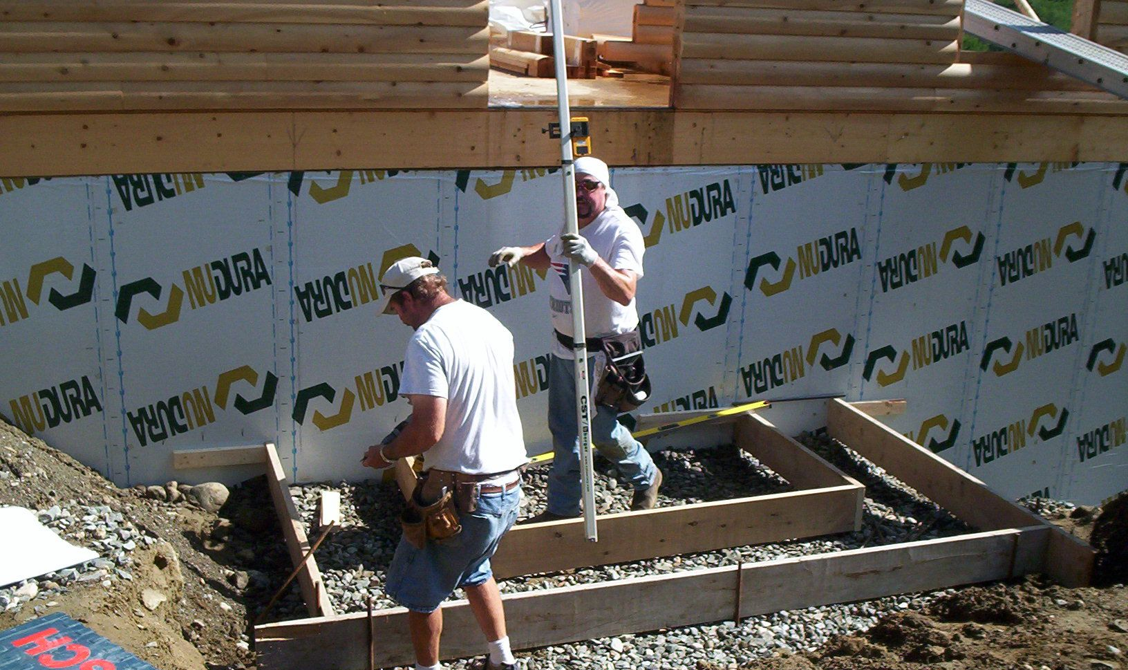 Two workers installing basement wall insulation at a construction site