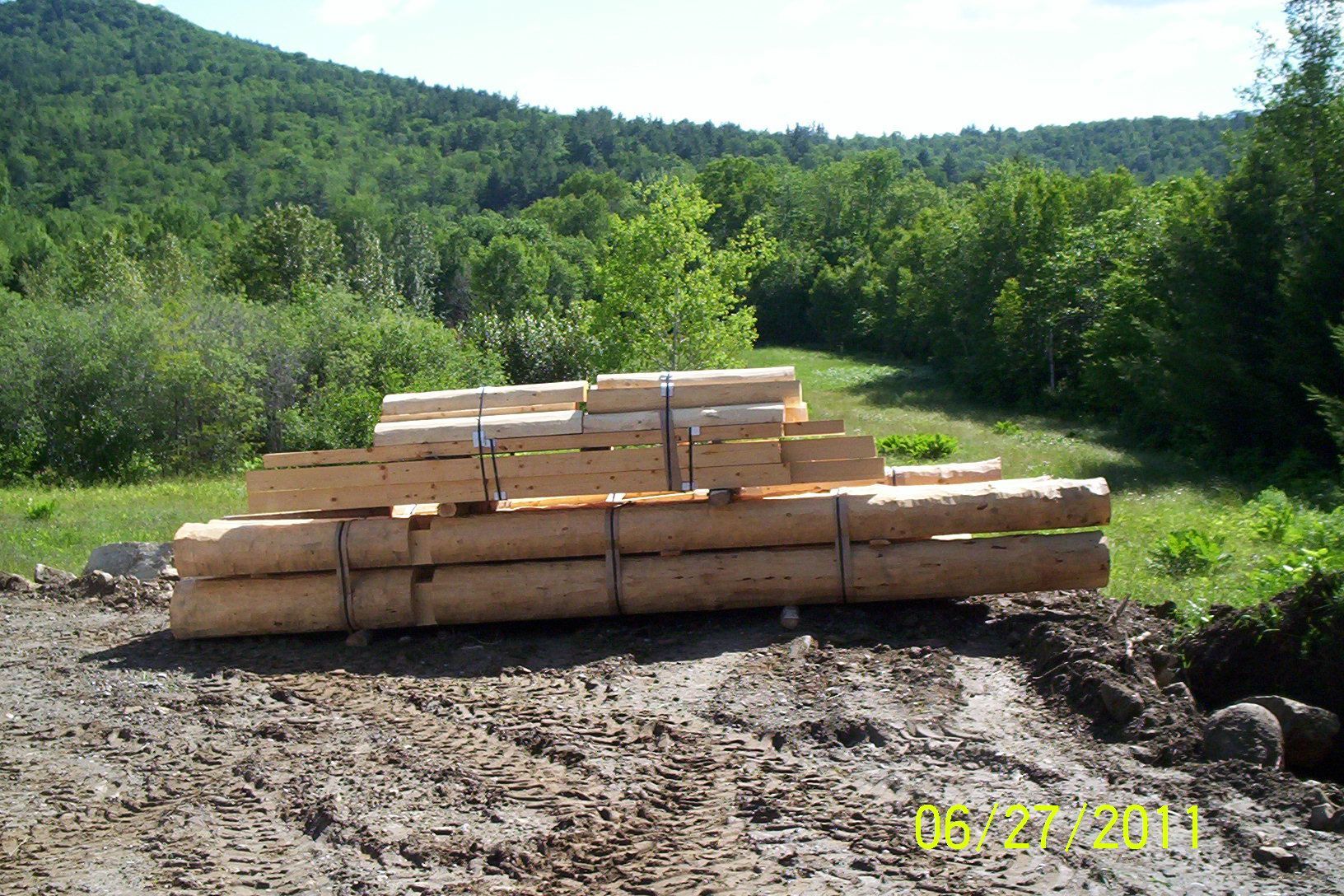 Stacked cut logs in a clearing with forested hills in the background