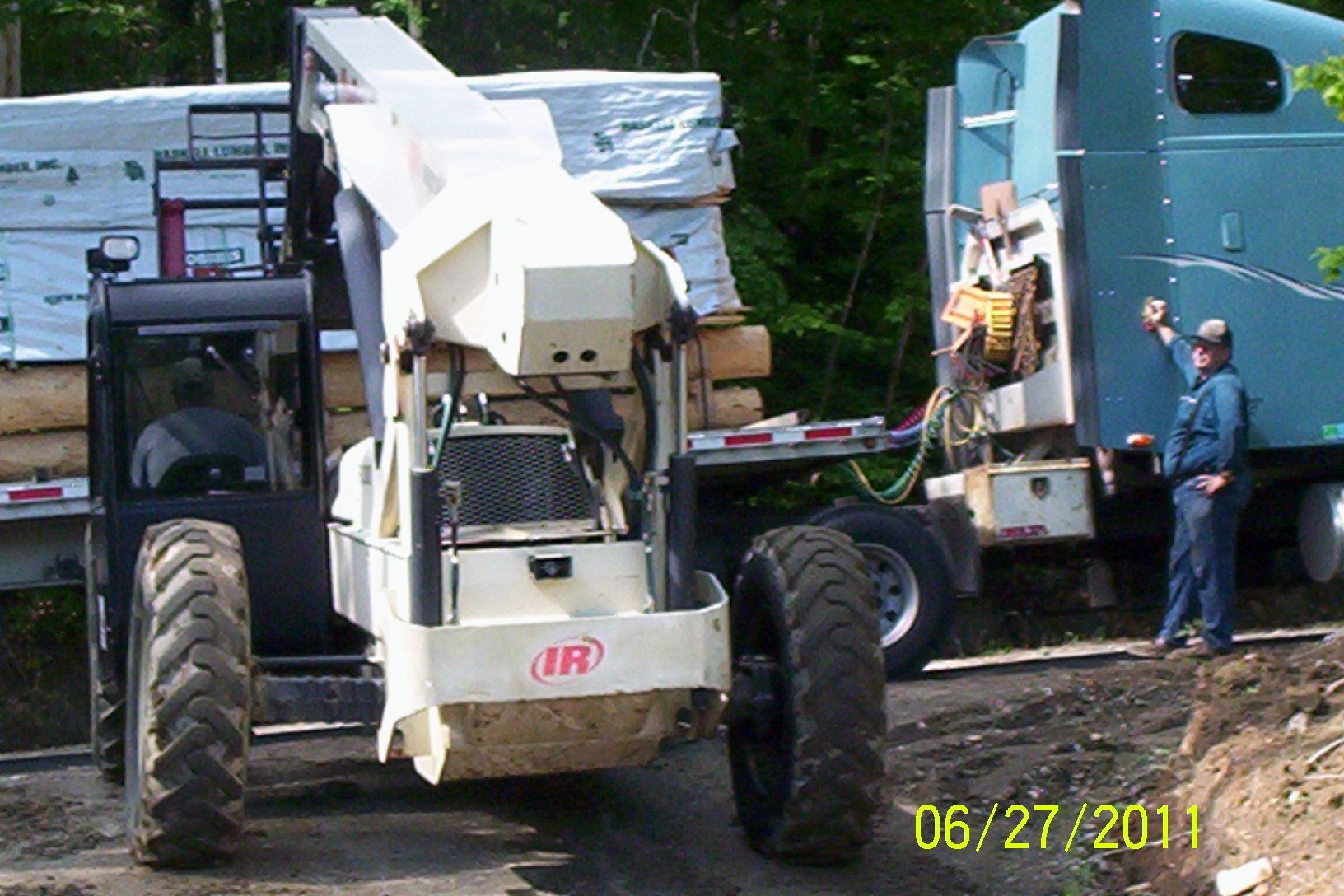 Construction lift loading materials onto a truck, with workers beside a green building.