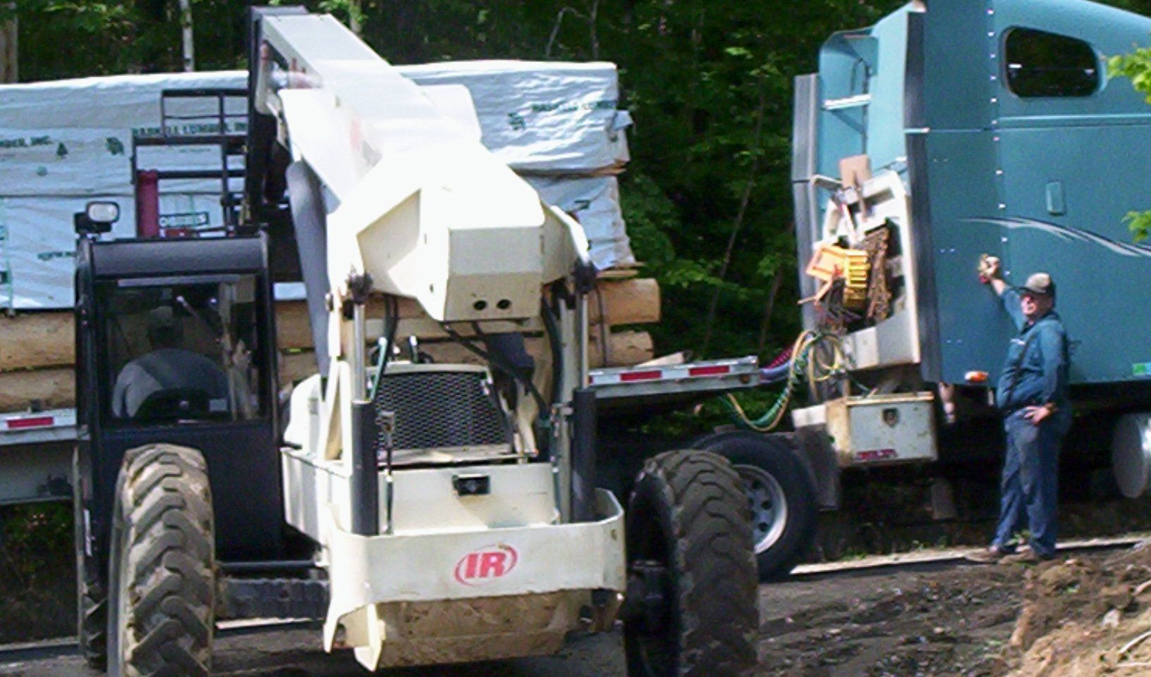 Construction equipment loading materials onto a trailer beside a green building, with workers nearby.