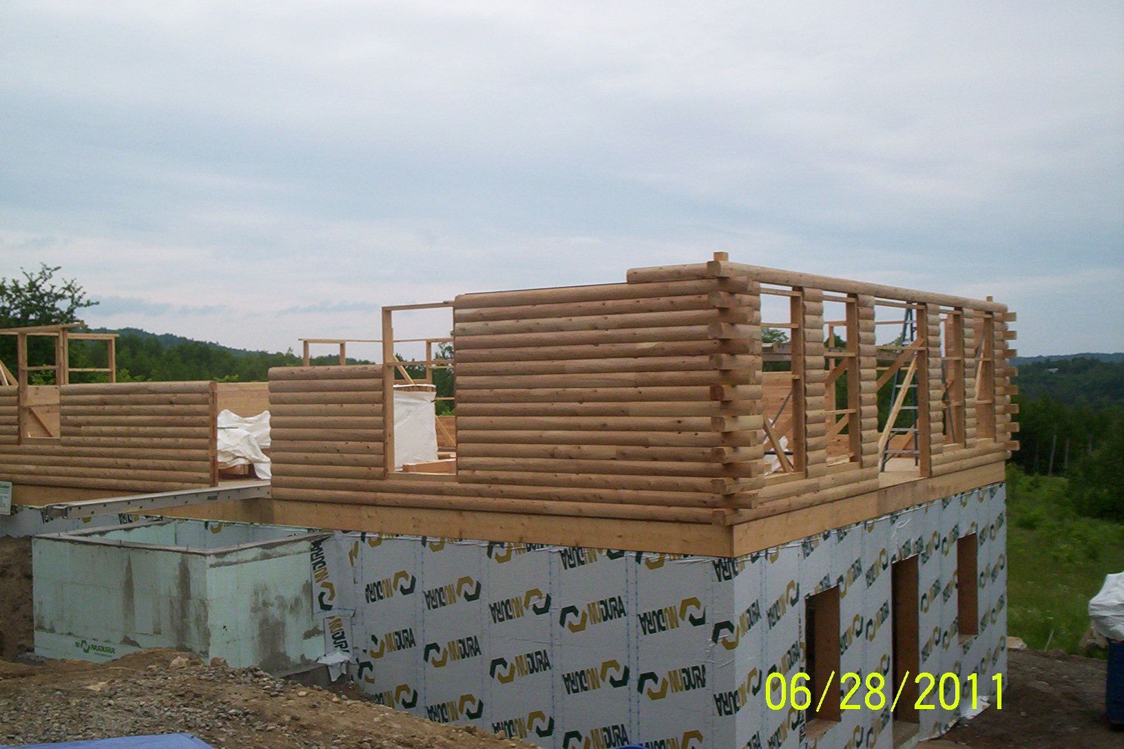 Partially built wooden house frame on a concrete foundation under a cloudy sky