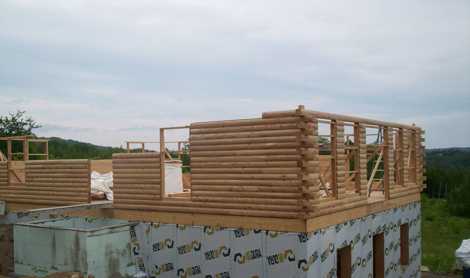 Partially built wooden house walls on a rooftop, with stacked lumber and cloudy sky in the background