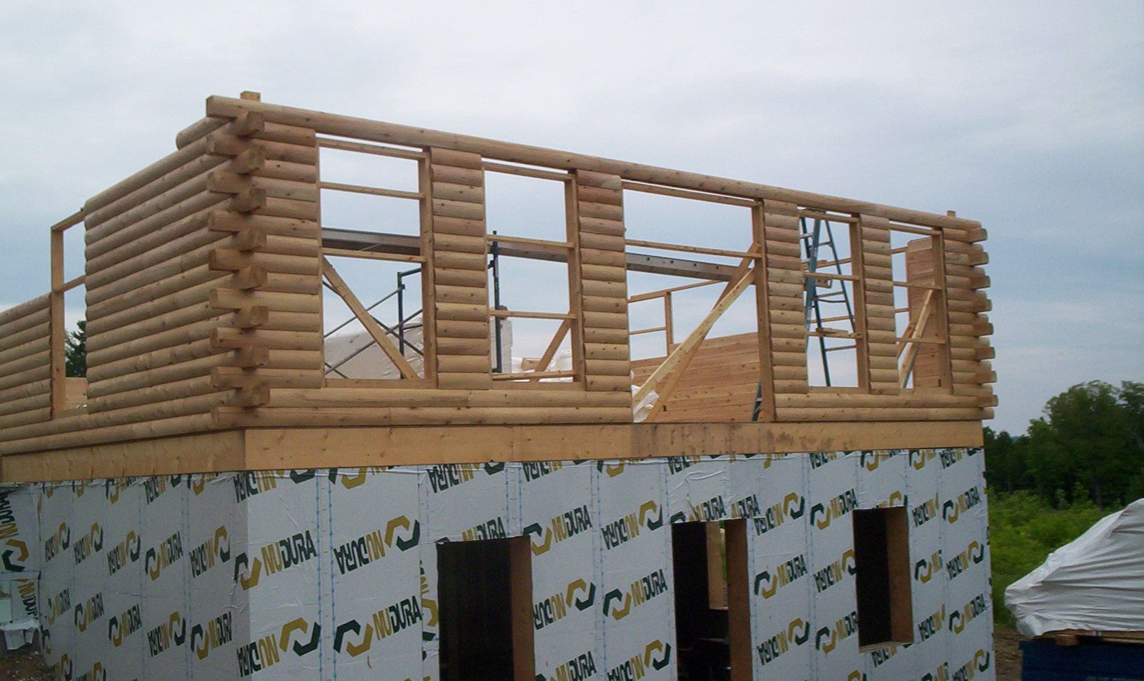 Partially built log house with unfinished upper walls and roof framing on a construction site