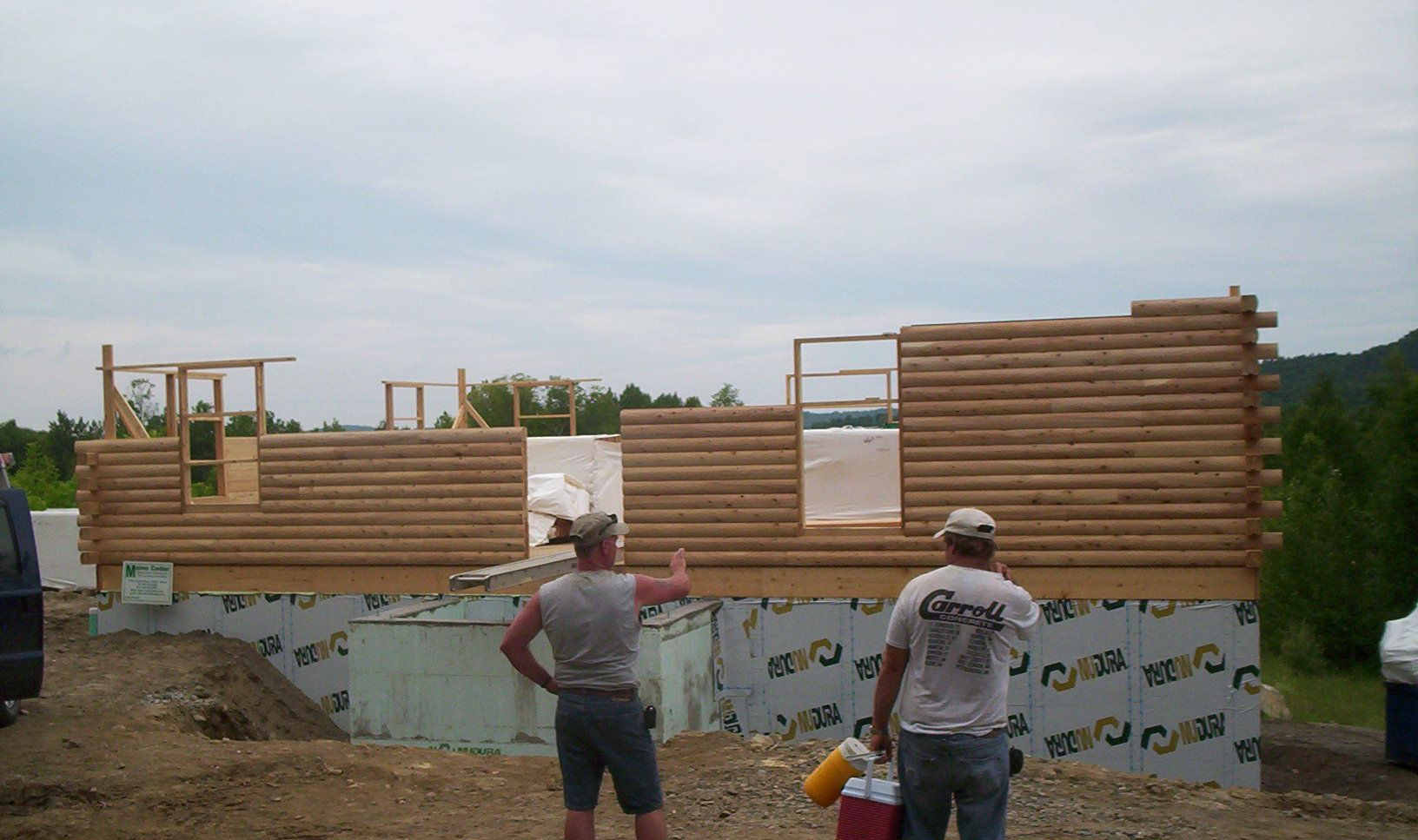 People working on a wooden wall frame at a construction site under a cloudy sky