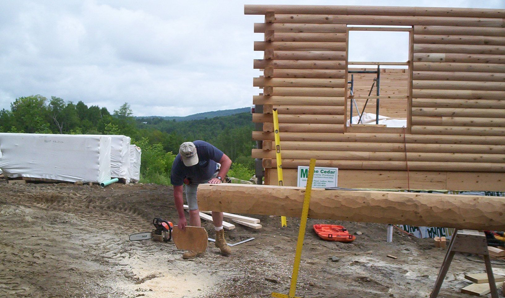 Worker sanding a log beam at a wooden cabin construction site