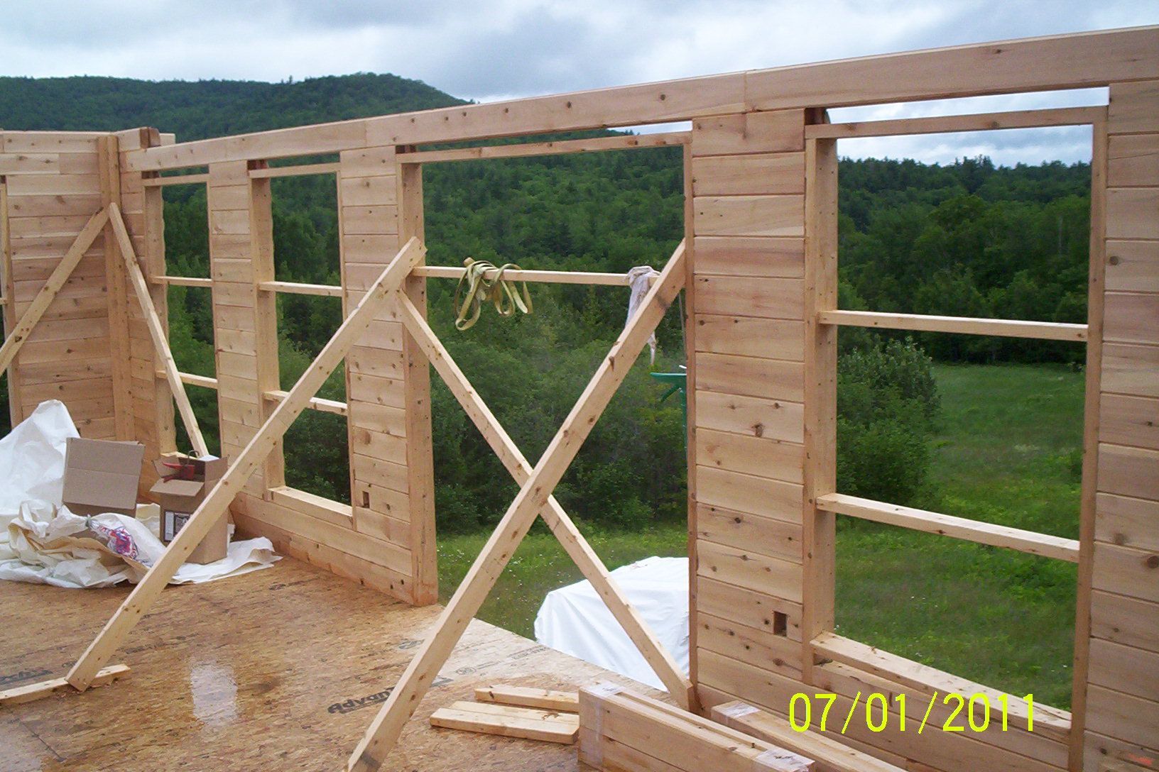 Wood-framed building under construction on a hillside, with temporary braces and open window and door openings.