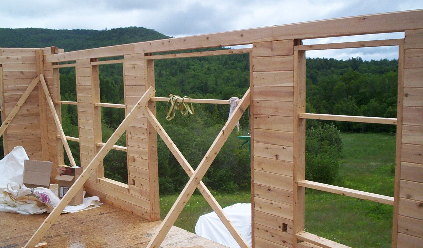Partially built wooden house frame with cross-bracing and forested hills in the background