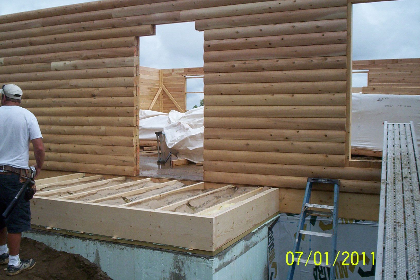 Two workers framing a log-cabin wall on a construction site with window openings.