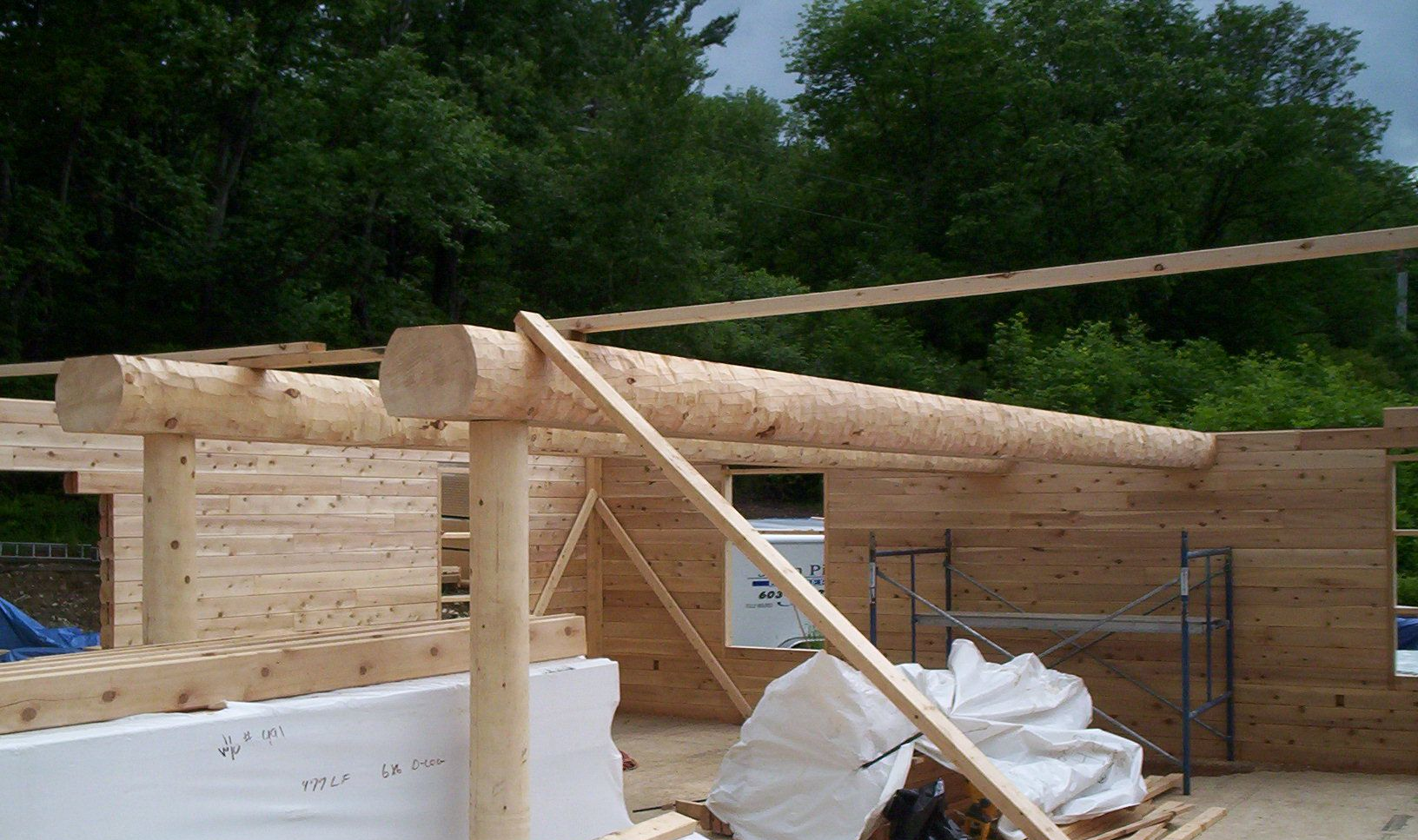 Partially built log cabin with timber walls, roof beams, and construction materials outdoors