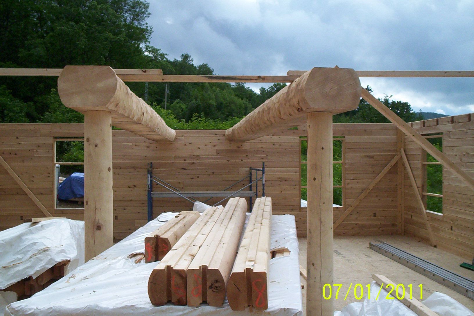 Partially built log cabin frame with stacked lumber and wooden walls in a rural outdoor setting