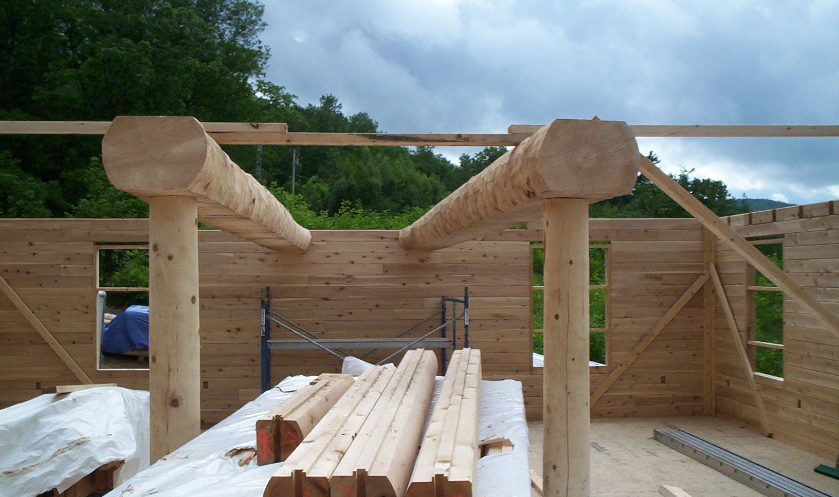 Wooden log cabin frame under construction with timber beams, posts, and stacked boards inside.
