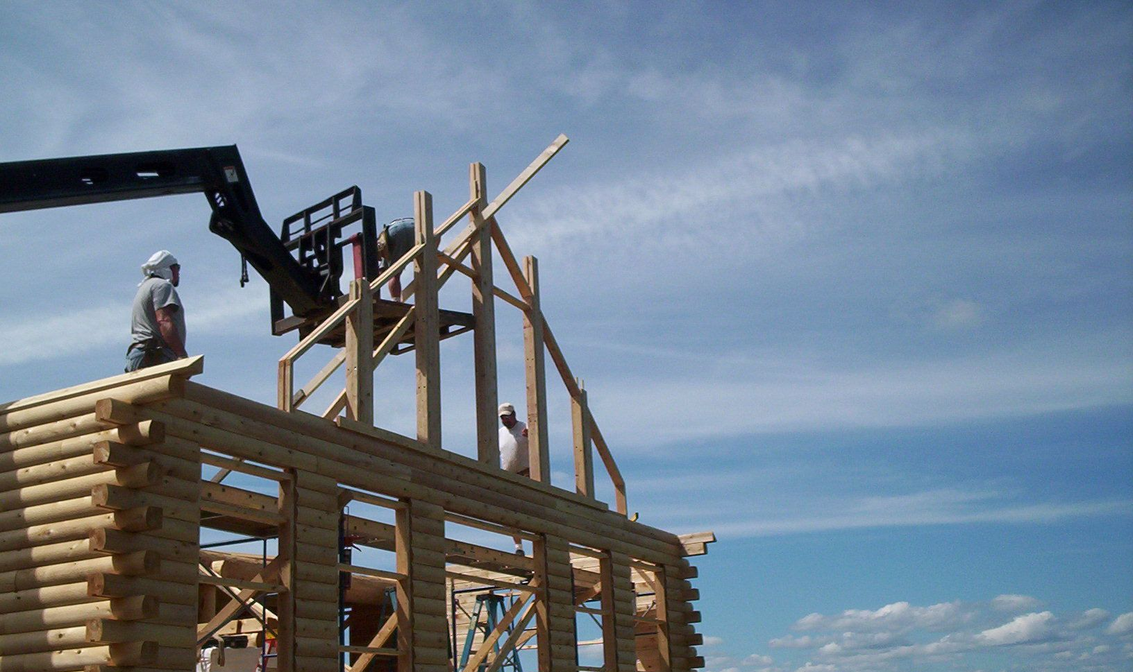 Worker framing a wooden house with a crane against a blue sky