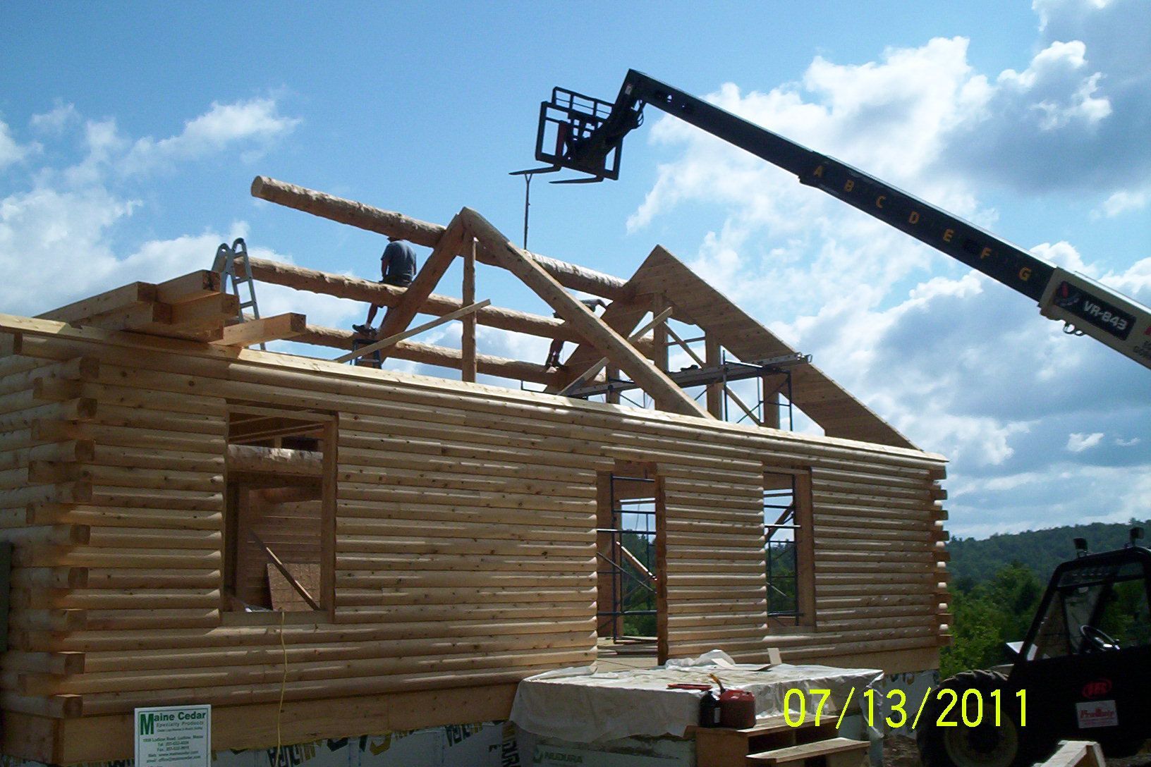 Partially built log cabin with roof trusses and a crane lifting beams on a construction site